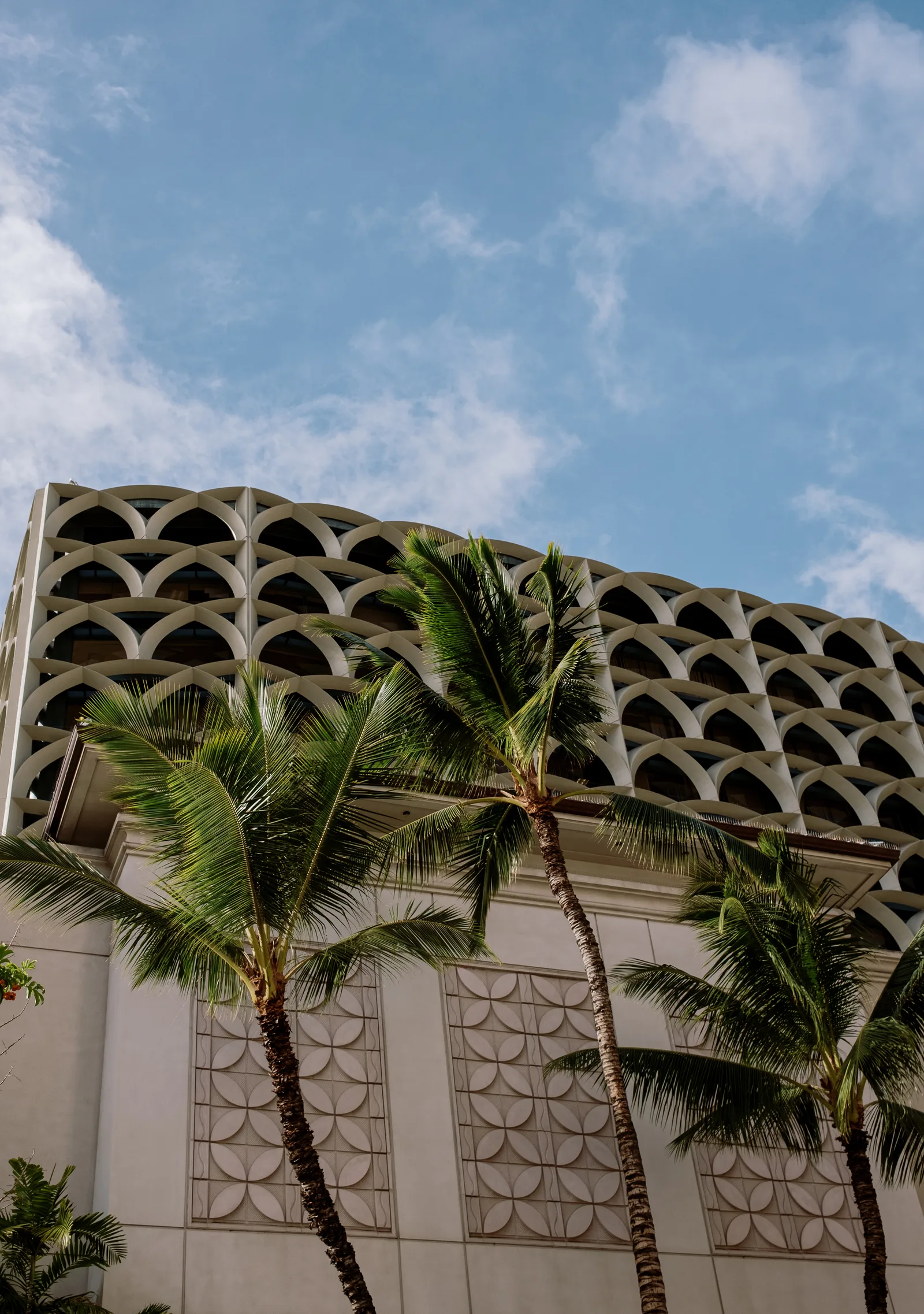 Palm trees in front of a building with a lattice arch parapet against blue sky, Honolulu