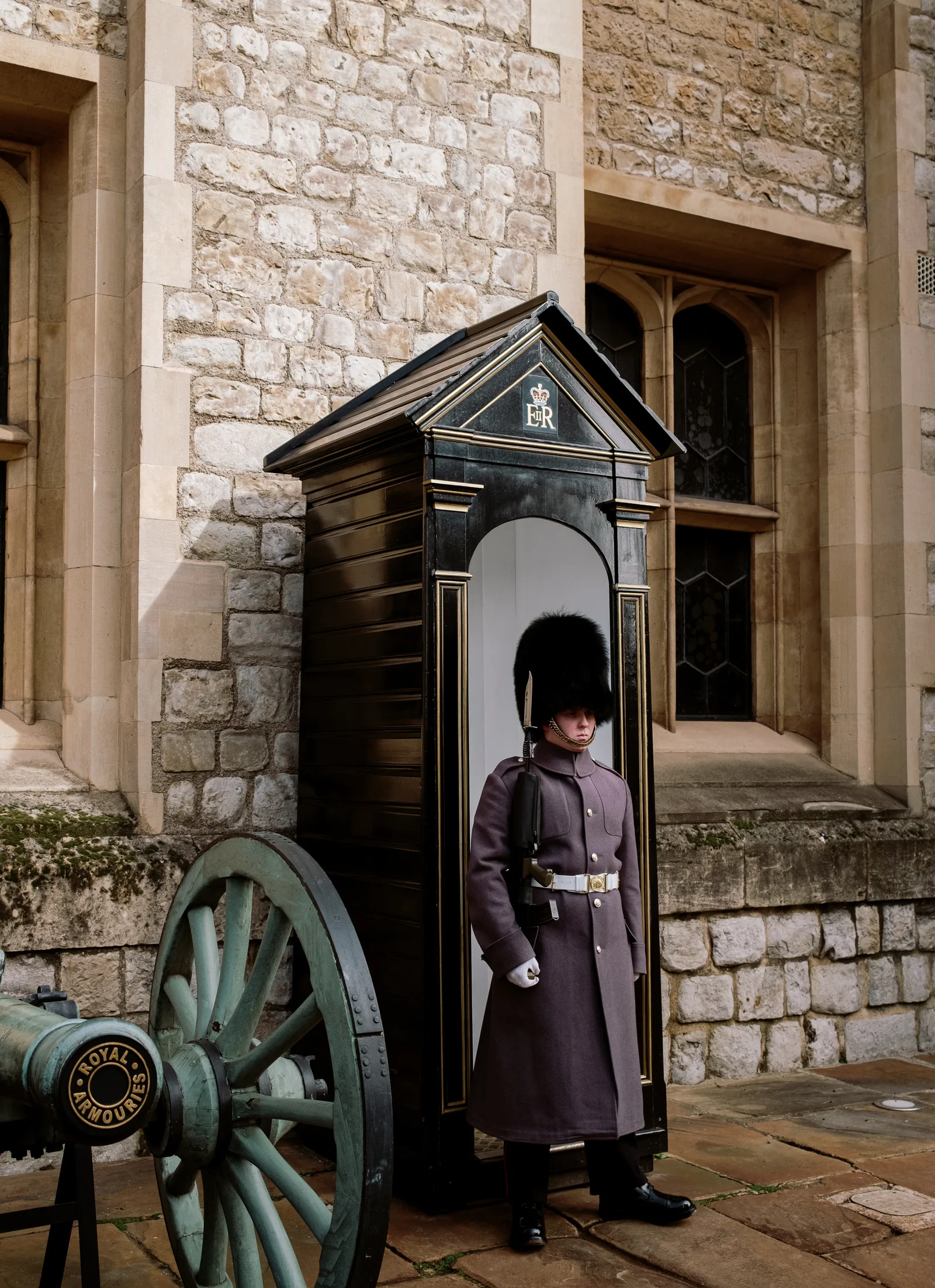 Guard in a long coat and bearskin hat beside a sentry box and an old cannon, London