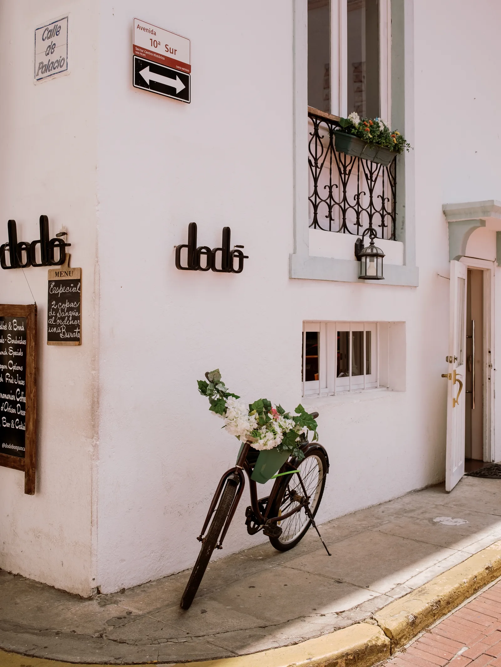 White corner cafe wall with a bicycle basket of flowers and a street sign, Panama City