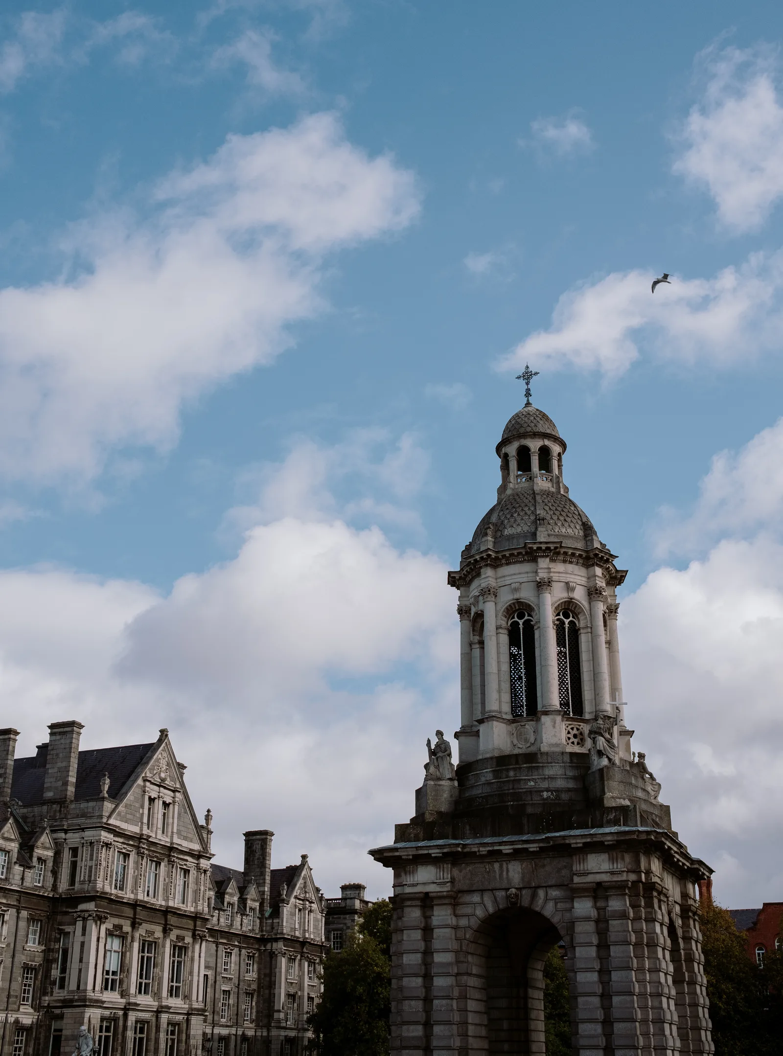 Bell tower of Trinity College Dublin beside a granite building under a blue, cloudy sky