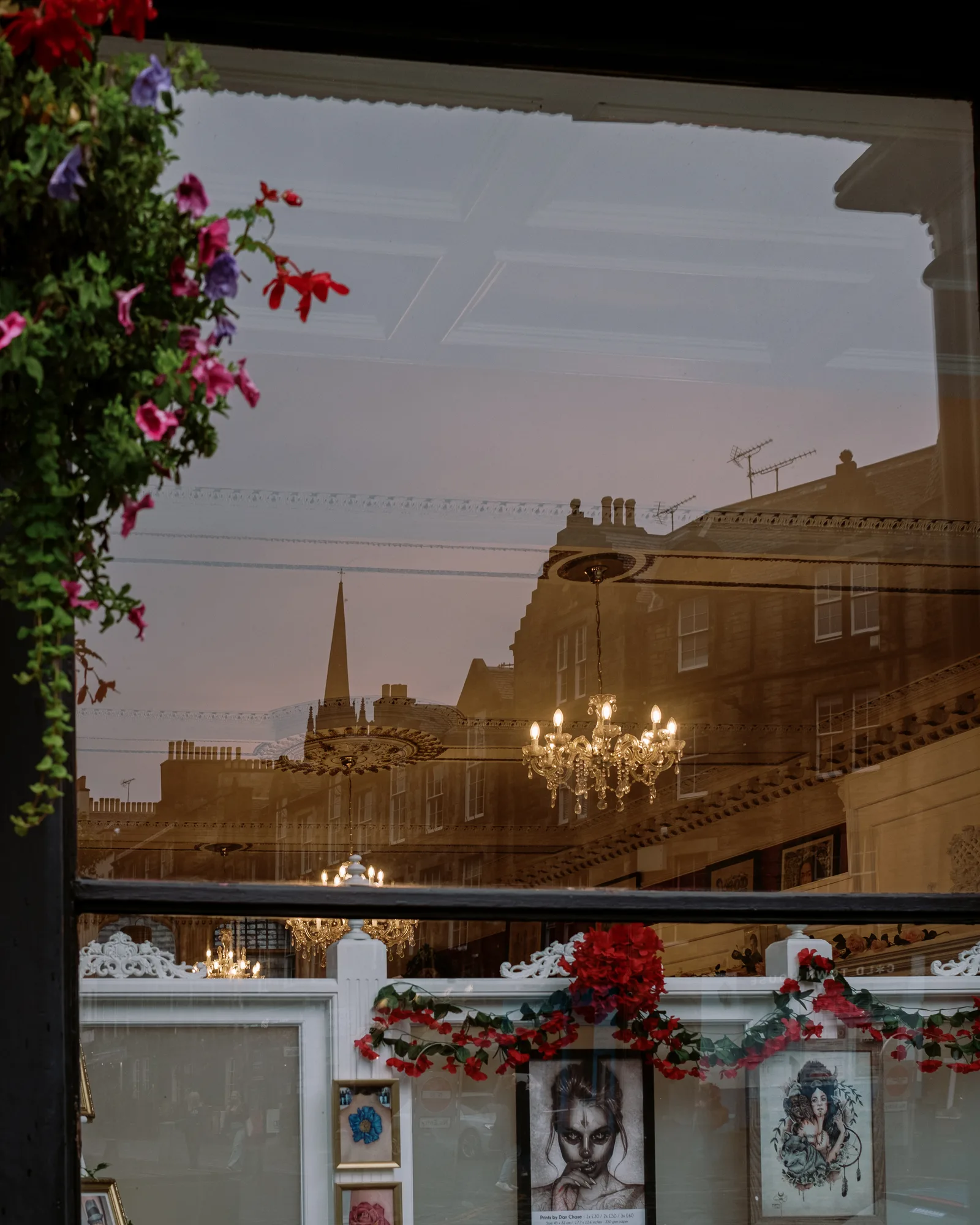Edinburgh street reflected in a shop window with a chandelier and hanging flowers at dusk