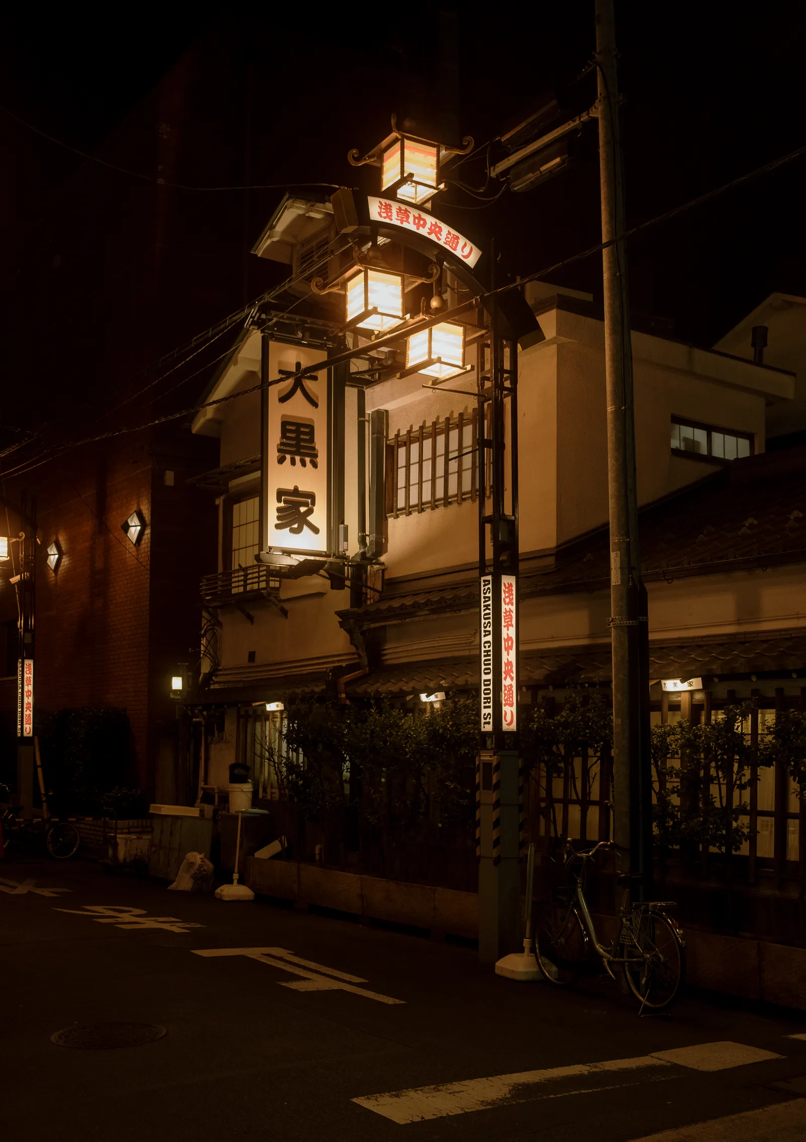 Lantern-lit wooden restaurant with a glowing kanji sign on a dark Tokyo street at night