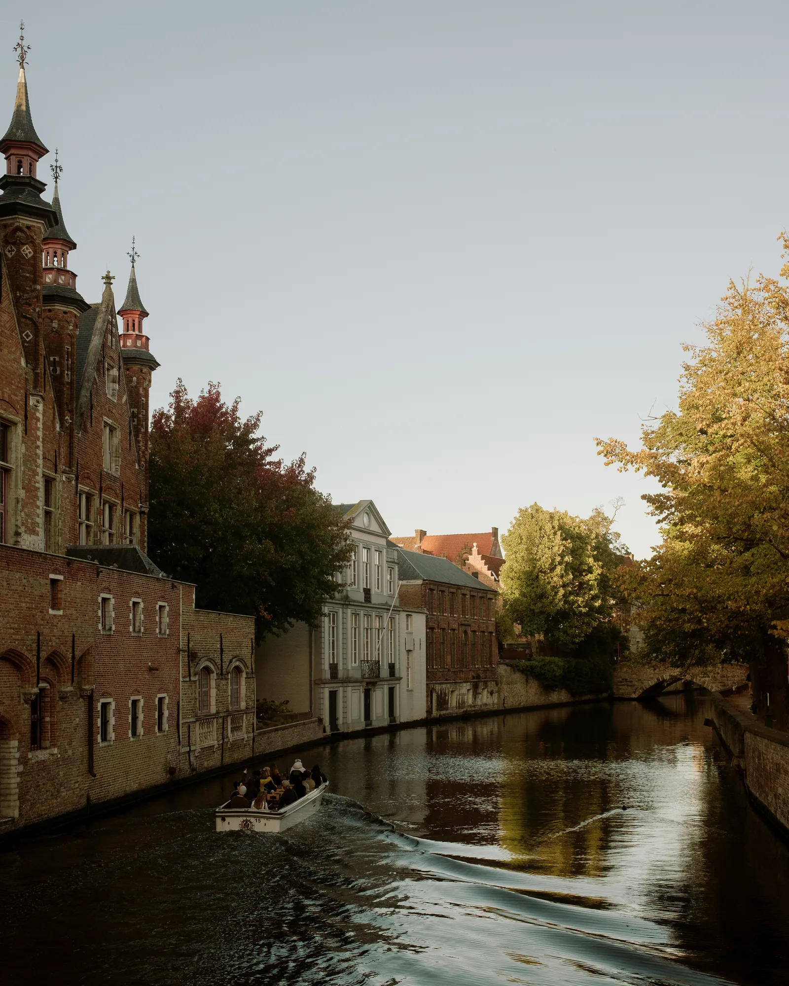 Tour boat leaving a wake on a Bruges canal beside brick buildings and turrets