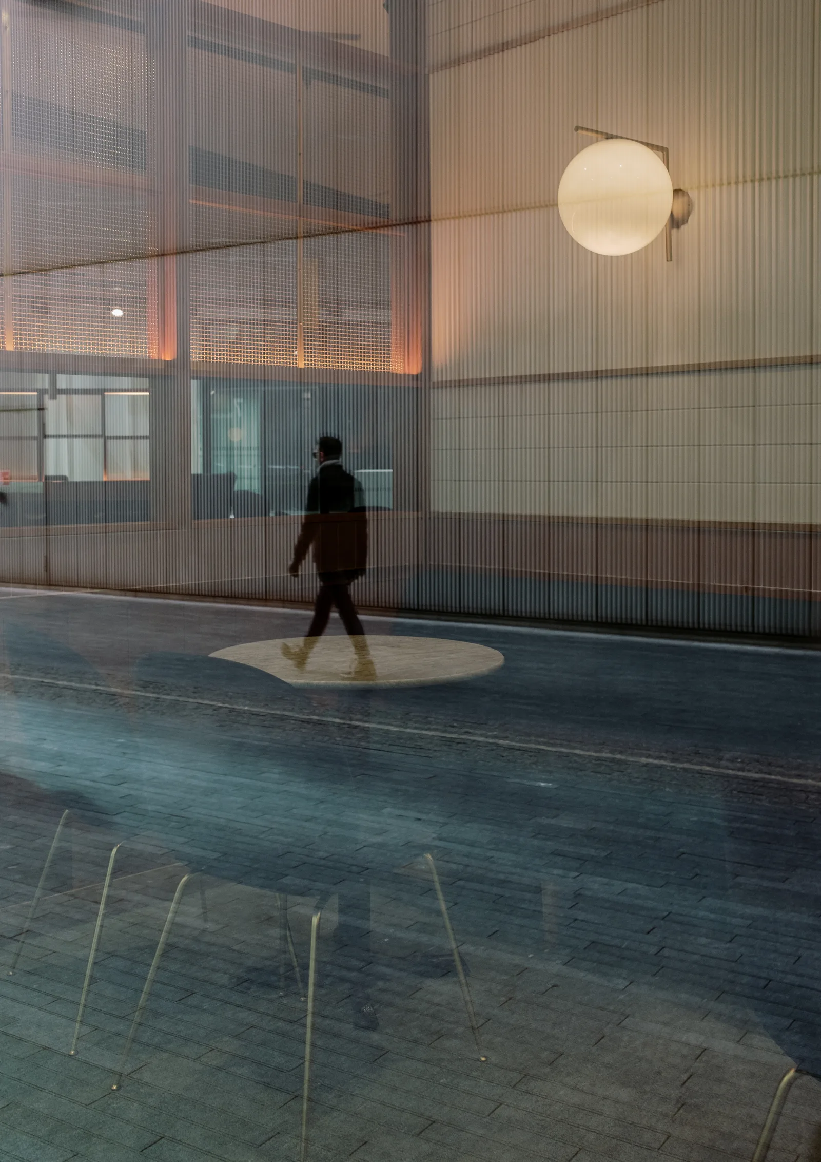 Silhouetted figure crossing a pool of light seen through glass in London