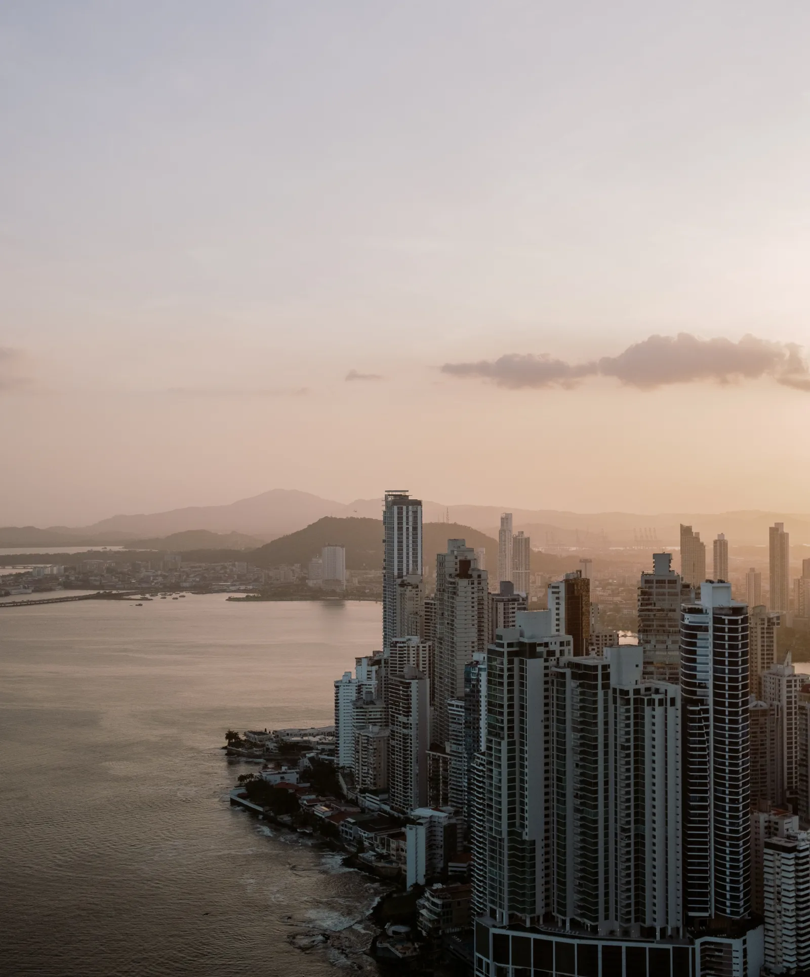 Panama City high-rises along the waterfront at sunset, hills and haze behind