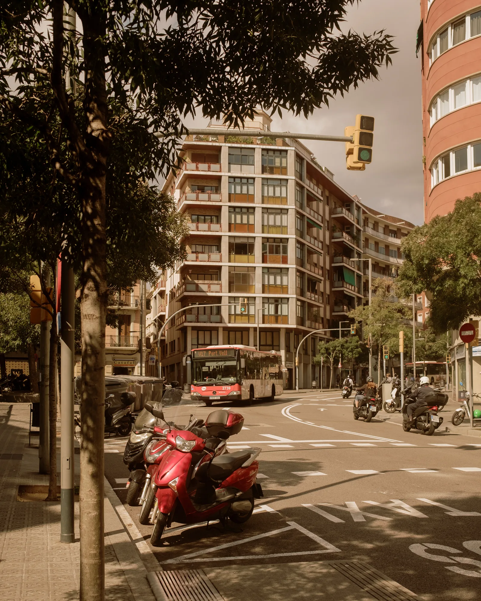 Barcelona street corner with parked red scooters, a city bus and an apartment block in afternoon light
