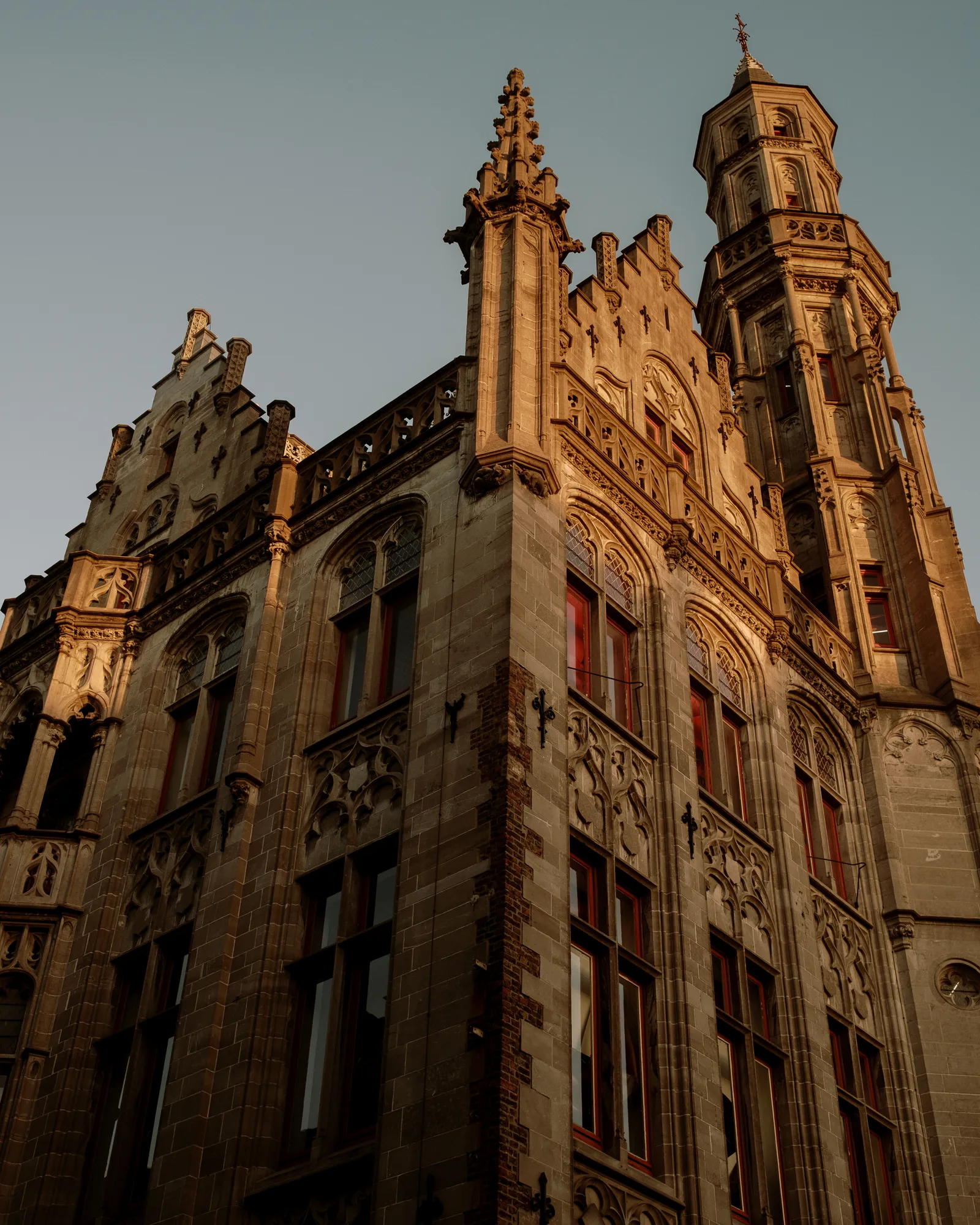 Stepped-gable Gothic building glowing in late light against a teal sky, Bruges