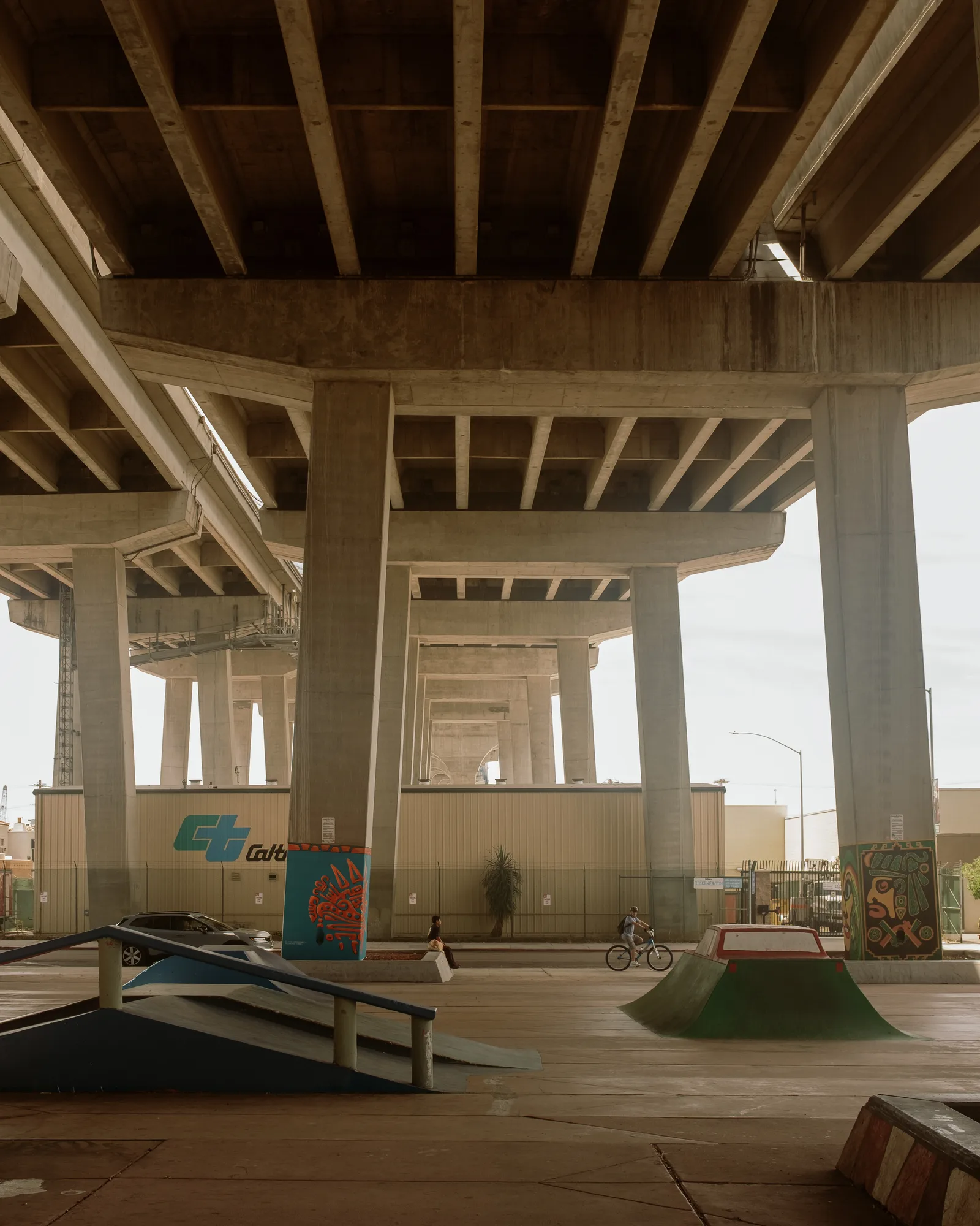 Concrete columns and beams under a freeway overpass with a skate ramp and painted murals, Barrio Logan