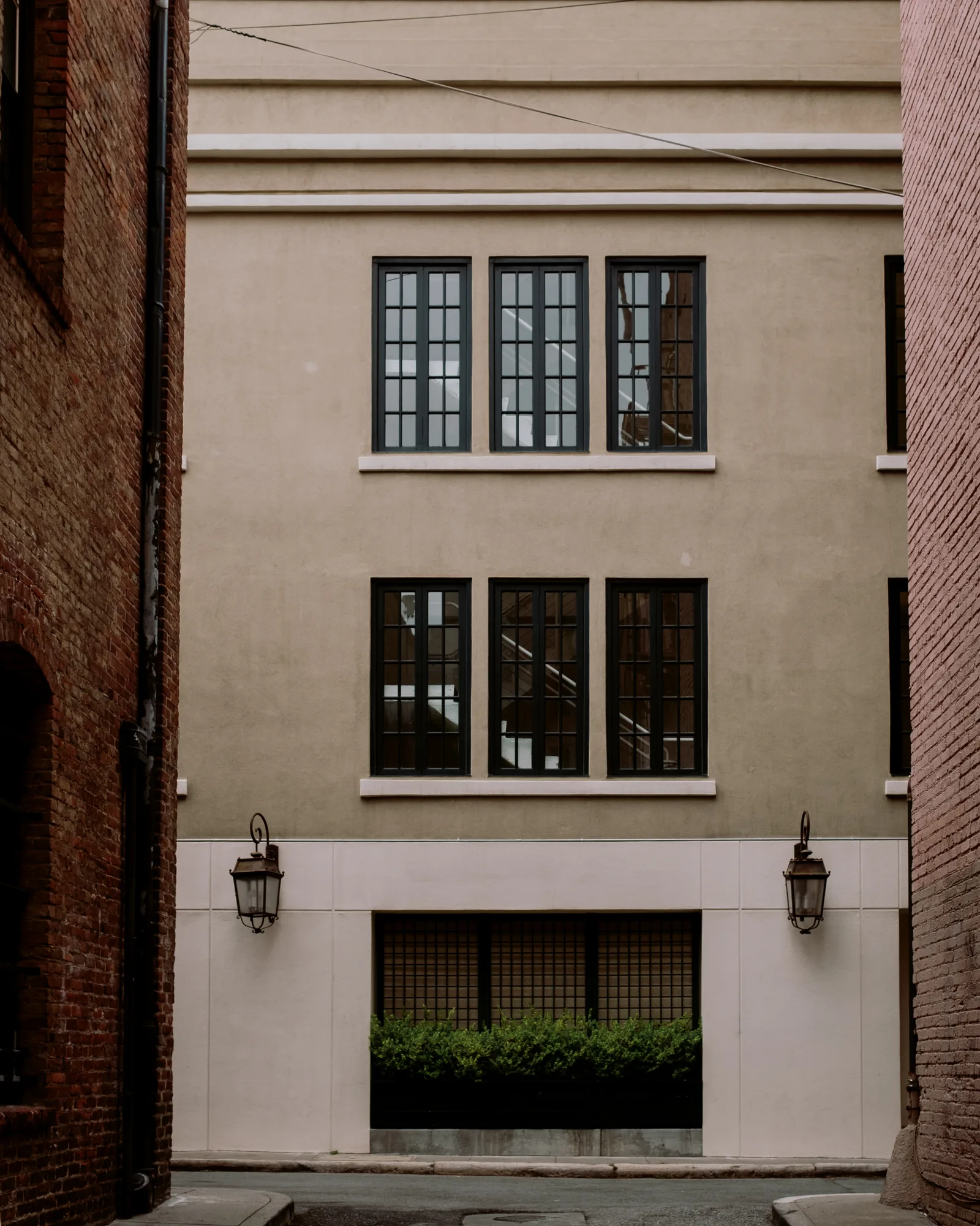 Tan building with black-framed windows and lanterns between brick walls, San Francisco