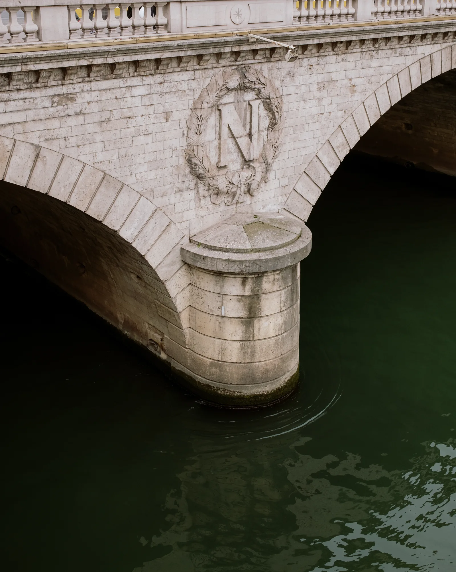 Napoleonic N emblem on a stone bridge pier above the dark green Seine, Paris