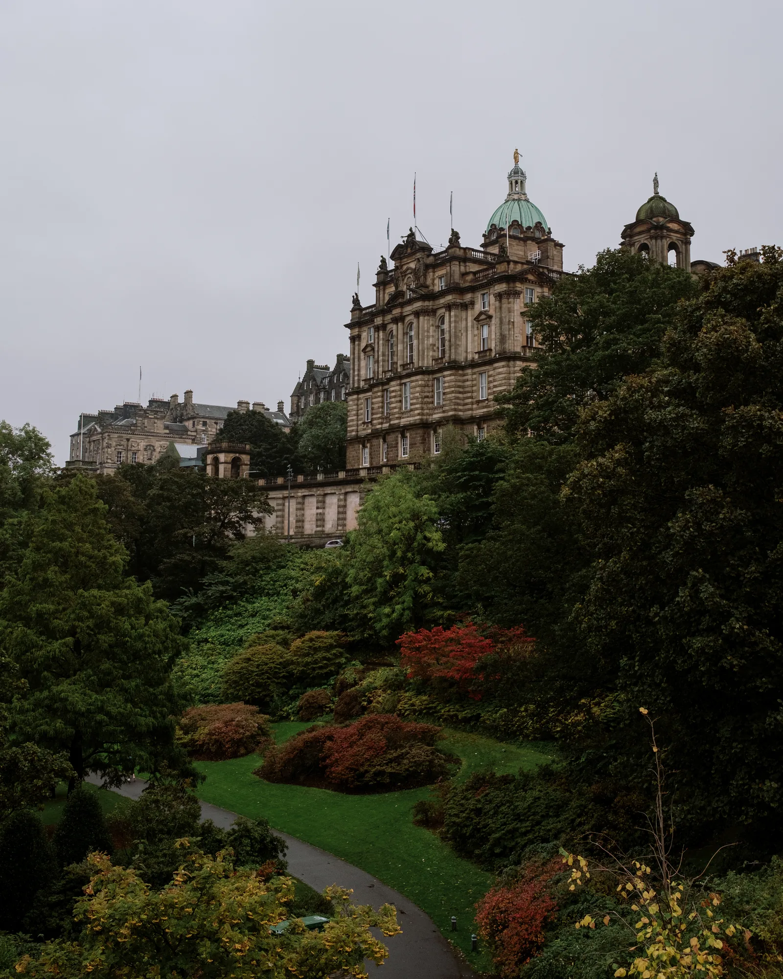 Edinburgh building rising above a hillside garden with red autumn shrubs and a winding path