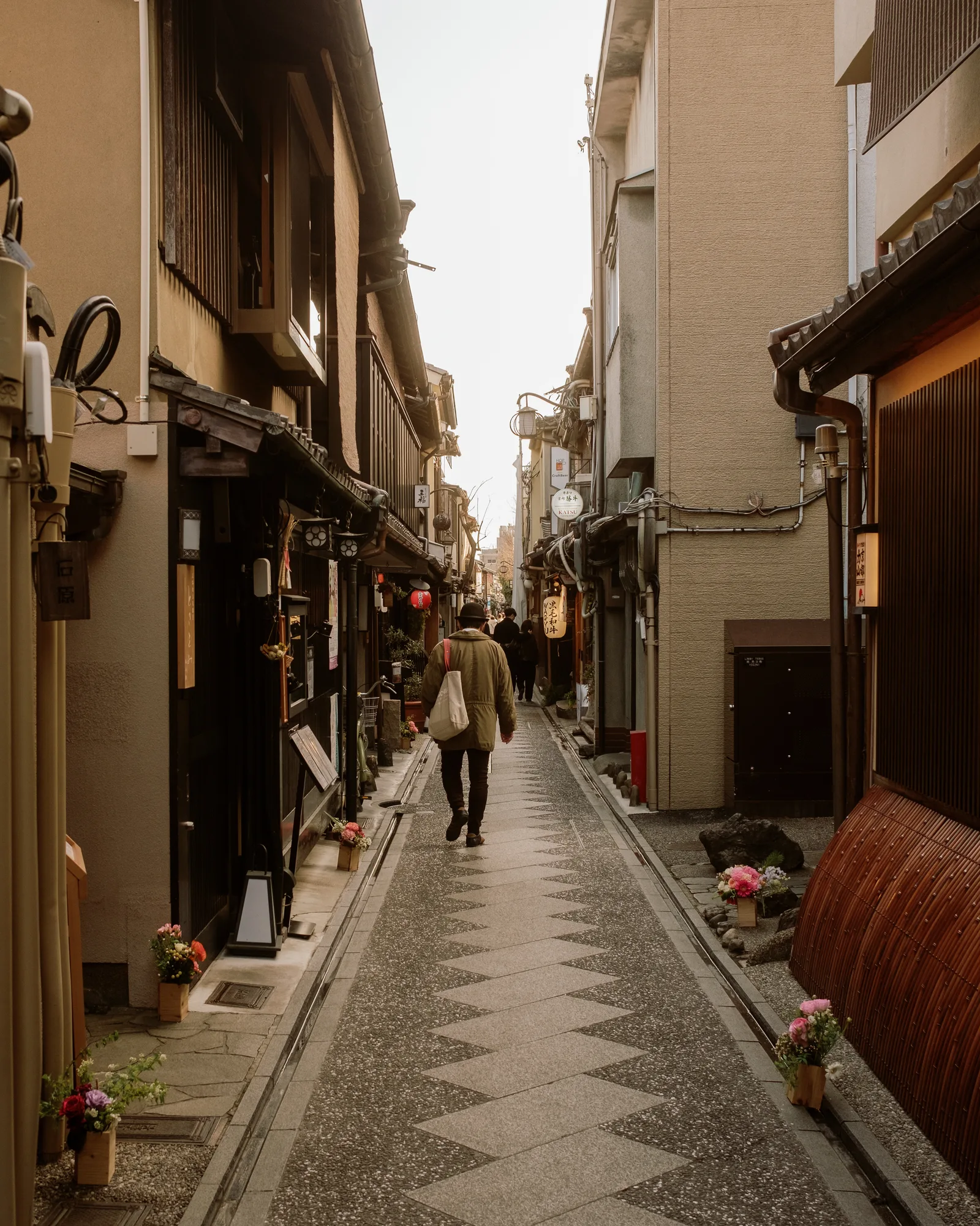 Person walking down a narrow Kyoto alley paved with a diamond pattern