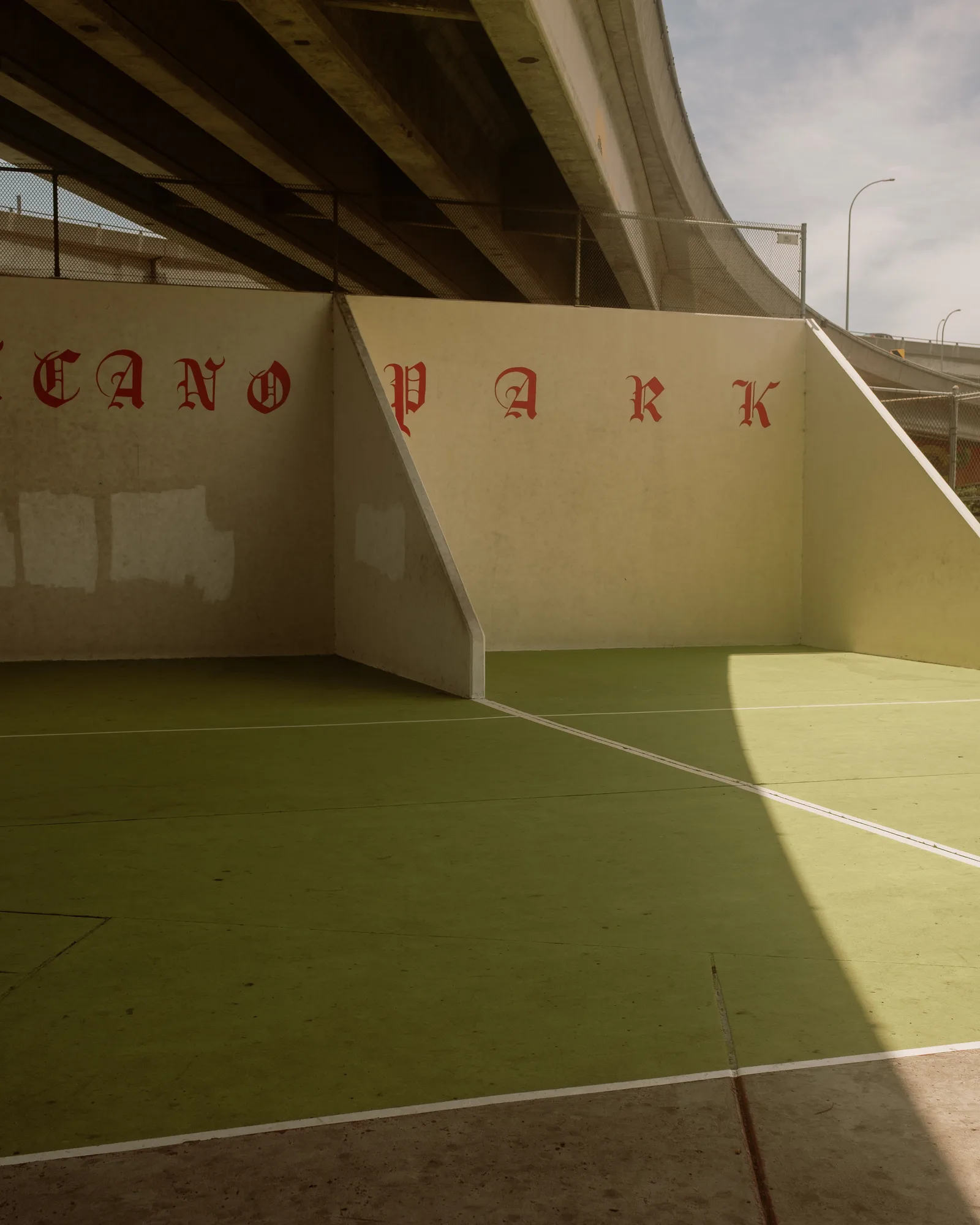 Angled court walls with red Chicano Park lettering and a shadow across a green floor, Barrio Logan