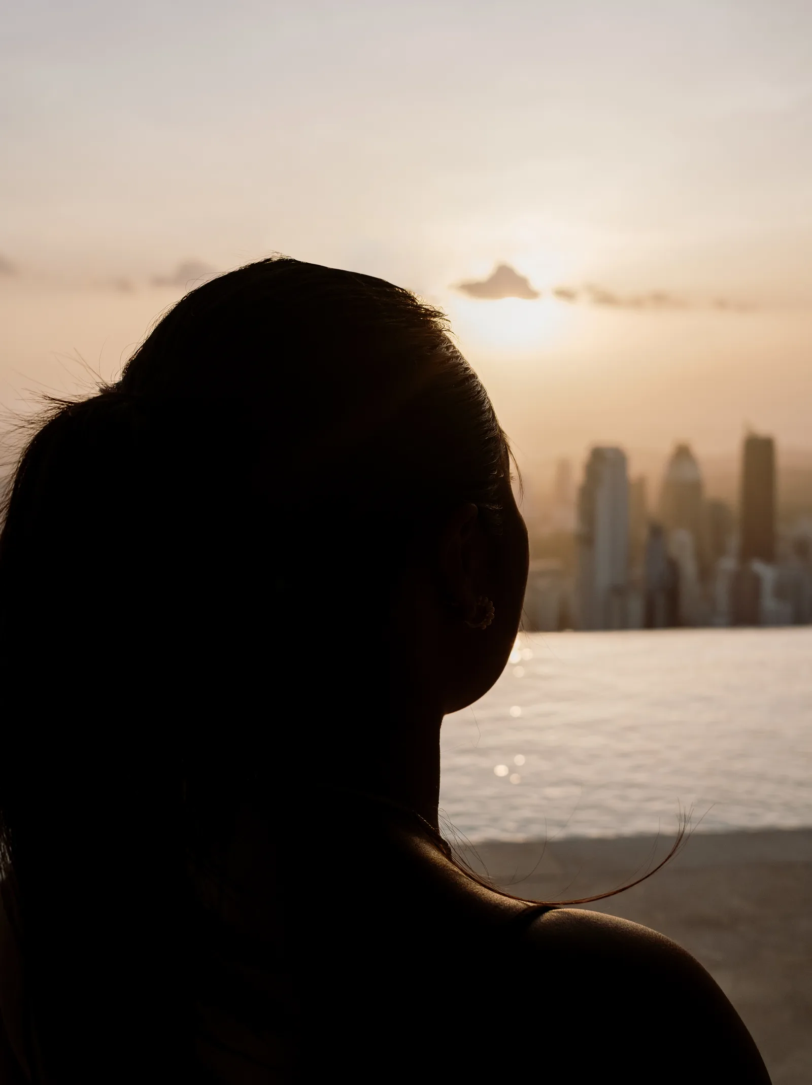 Silhouette of a woman's head against the setting sun and the Panama City skyline