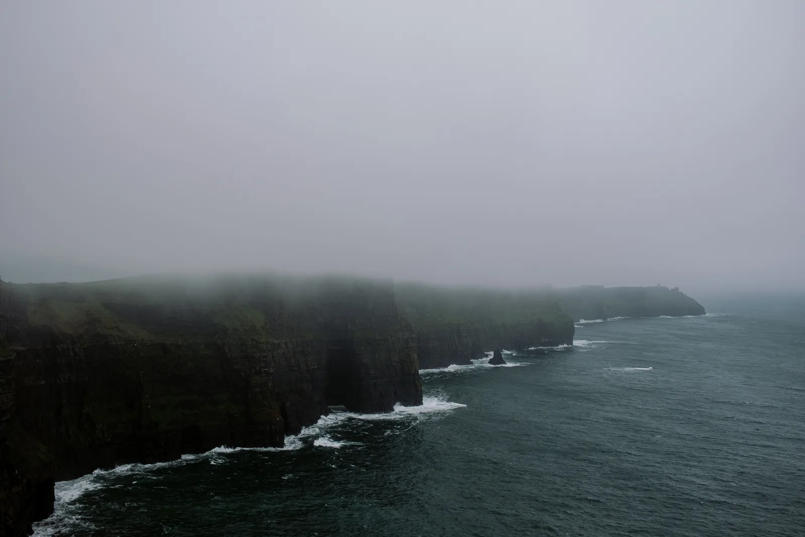 Misty Cliffs of Moher with waves breaking at their base, Ireland