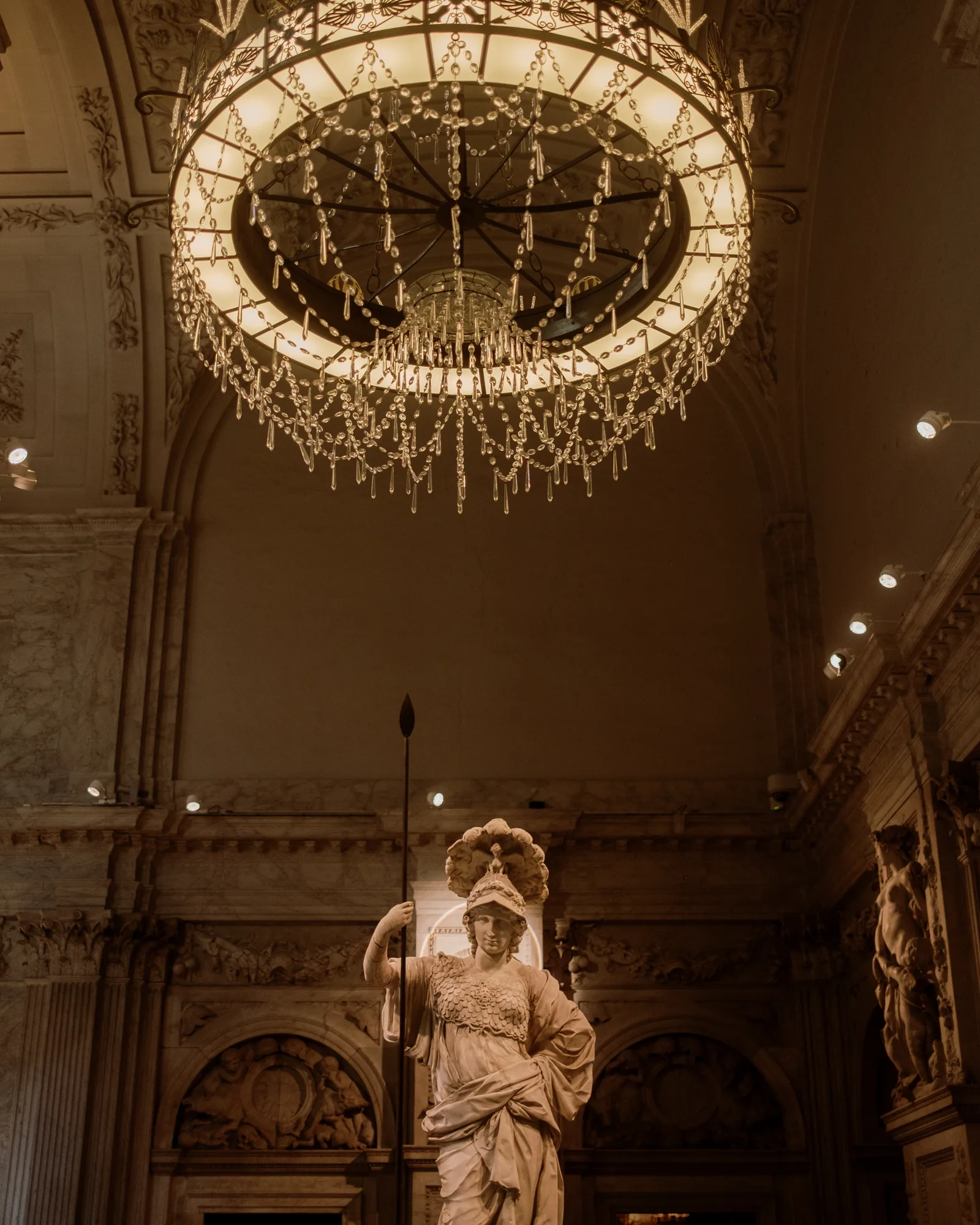 Vaulted Amsterdam hall with a large crystal chandelier above a statue of a helmeted figure