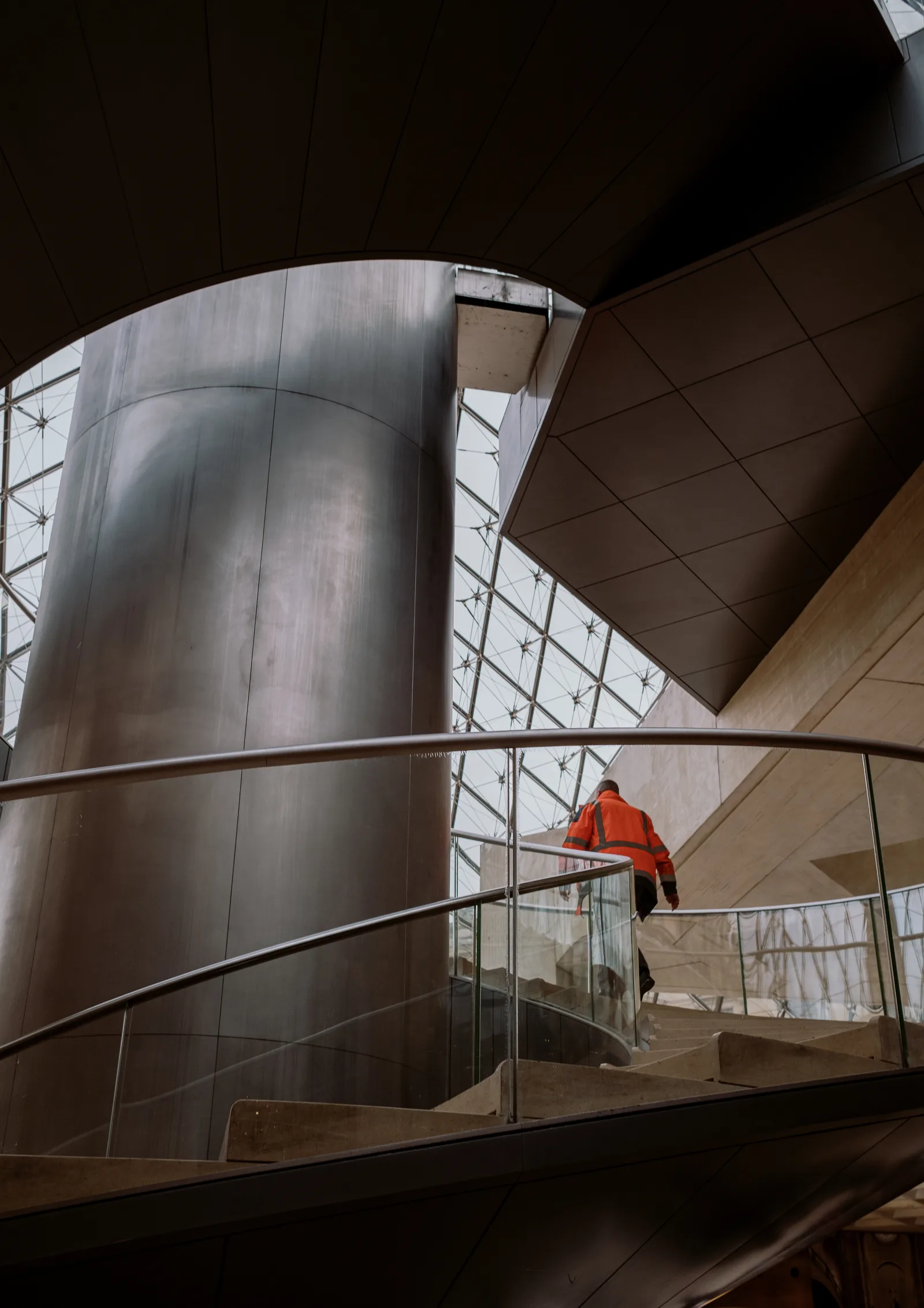 Person in orange climbing a spiral staircase inside the Louvre's glass pyramid, Paris
