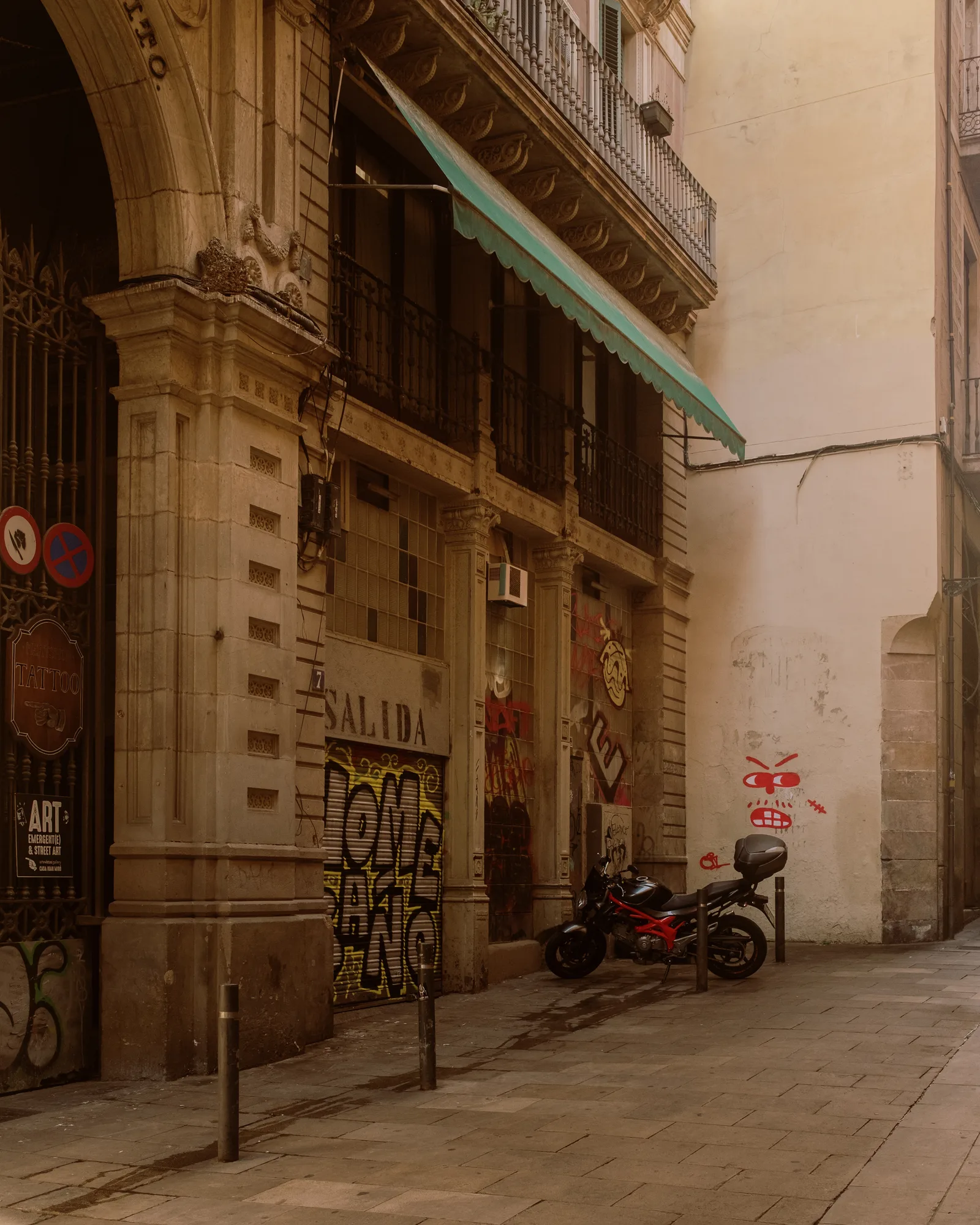 Barcelona side street with a grand arched doorway, a green awning and a parked motorcycle