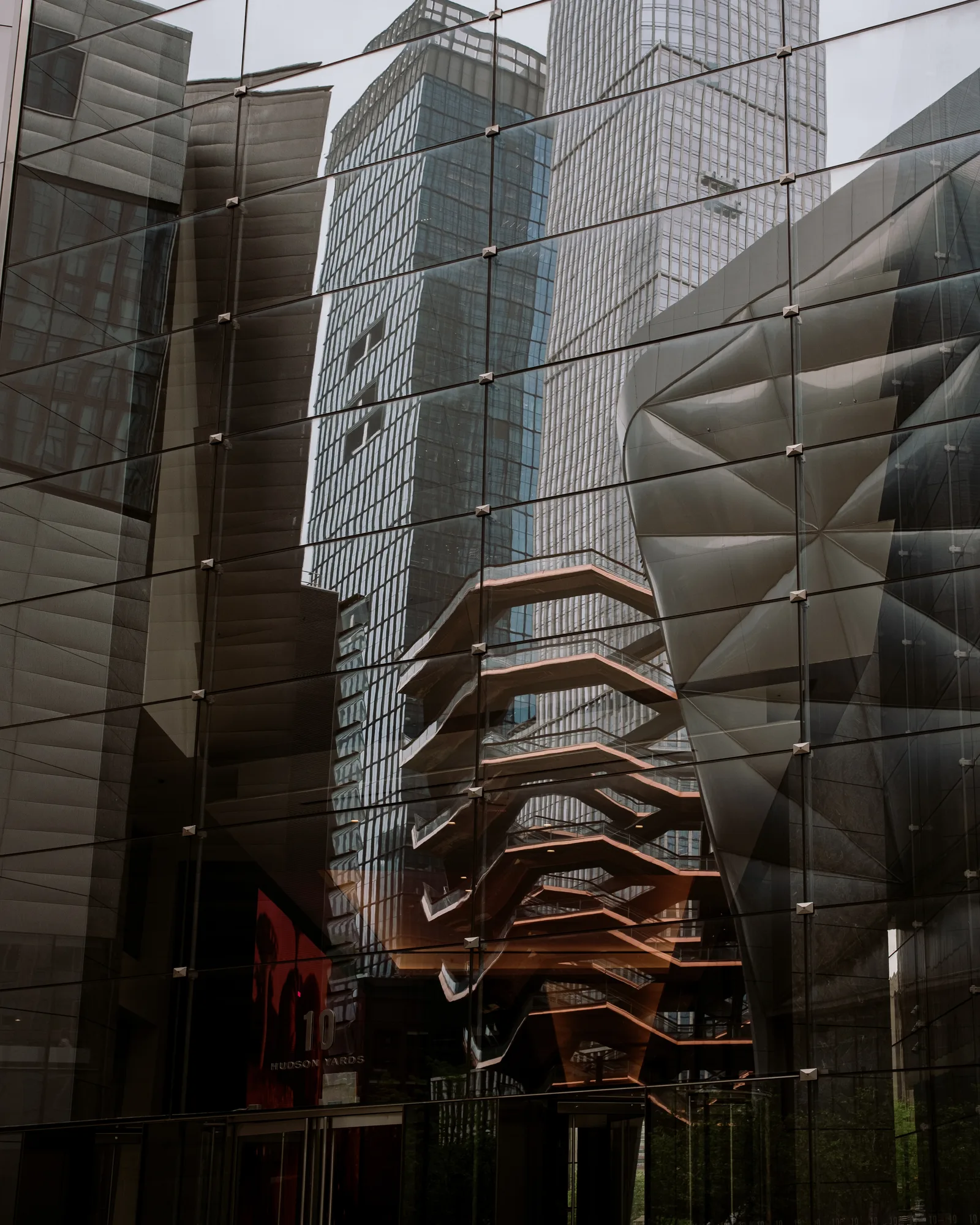 Glass towers and the Vessel structure reflected in a facade at Hudson Yards, New York