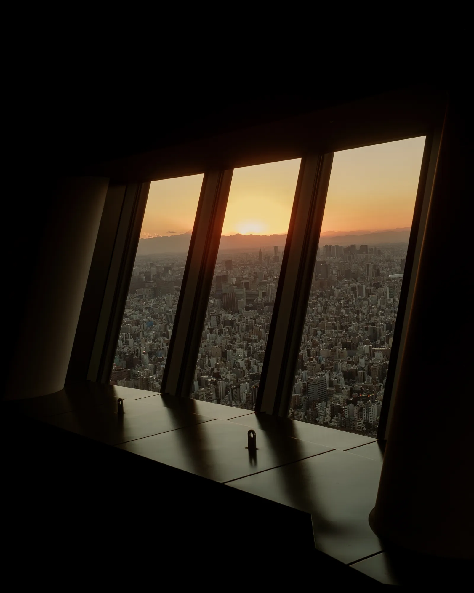 Sun setting over Tokyo seen through angled windows of a dark observation room