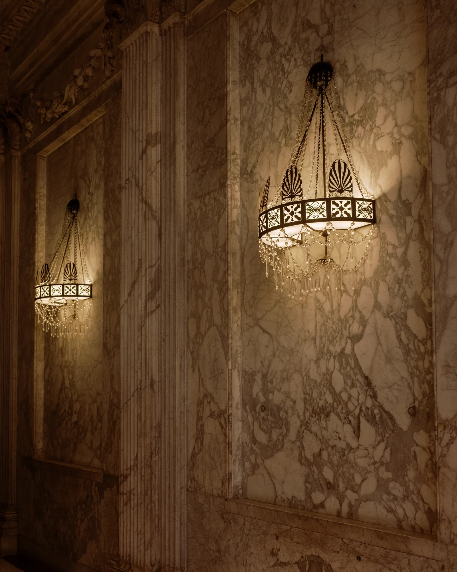 Two glowing vintage sconce lamps on a veined marble wall in Amsterdam
