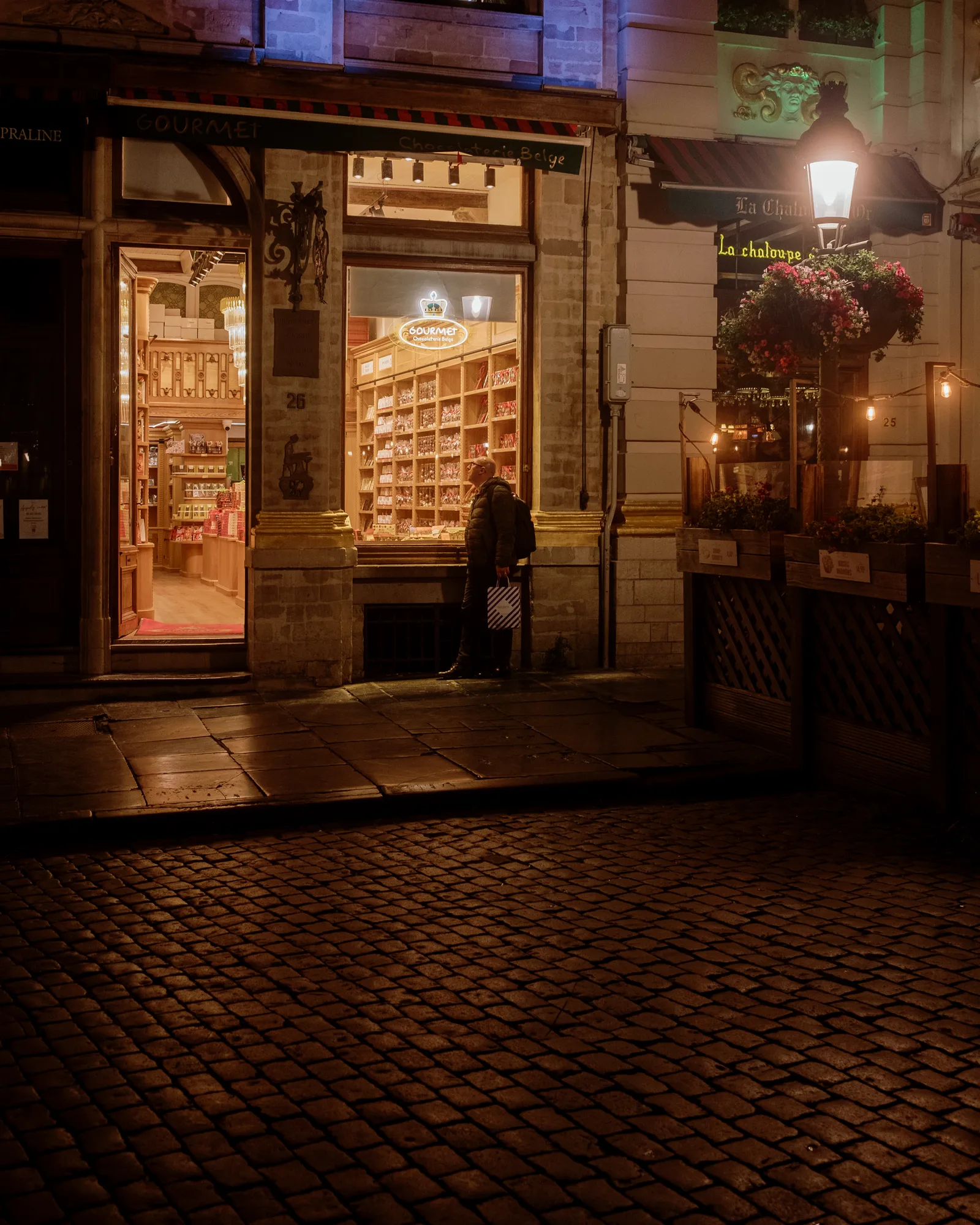 Lit shop window on a cobbled Brussels street at night, shelves glowing inside