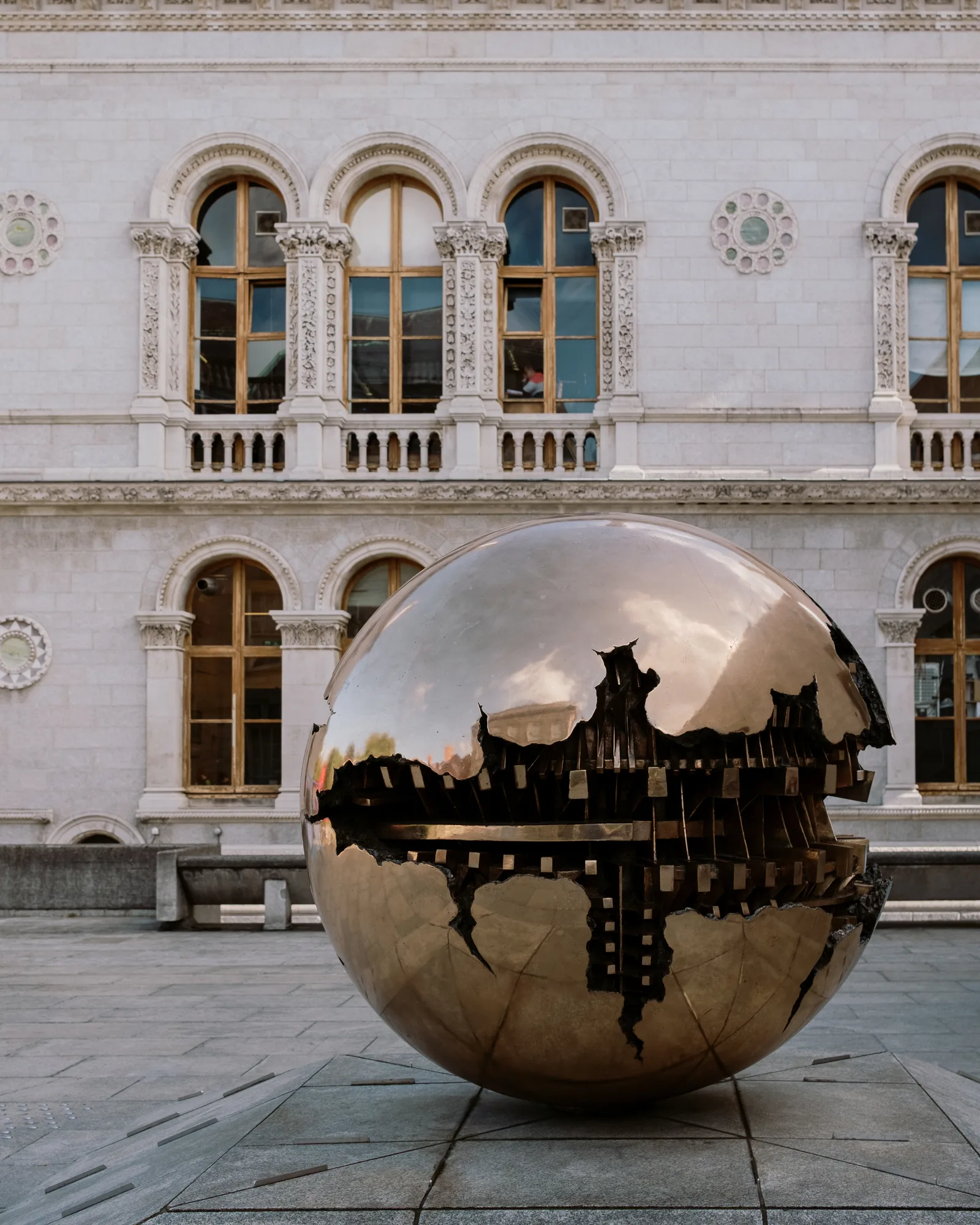 Bronze sphere sculpture reflecting a Trinity College Dublin courtyard and arched windows