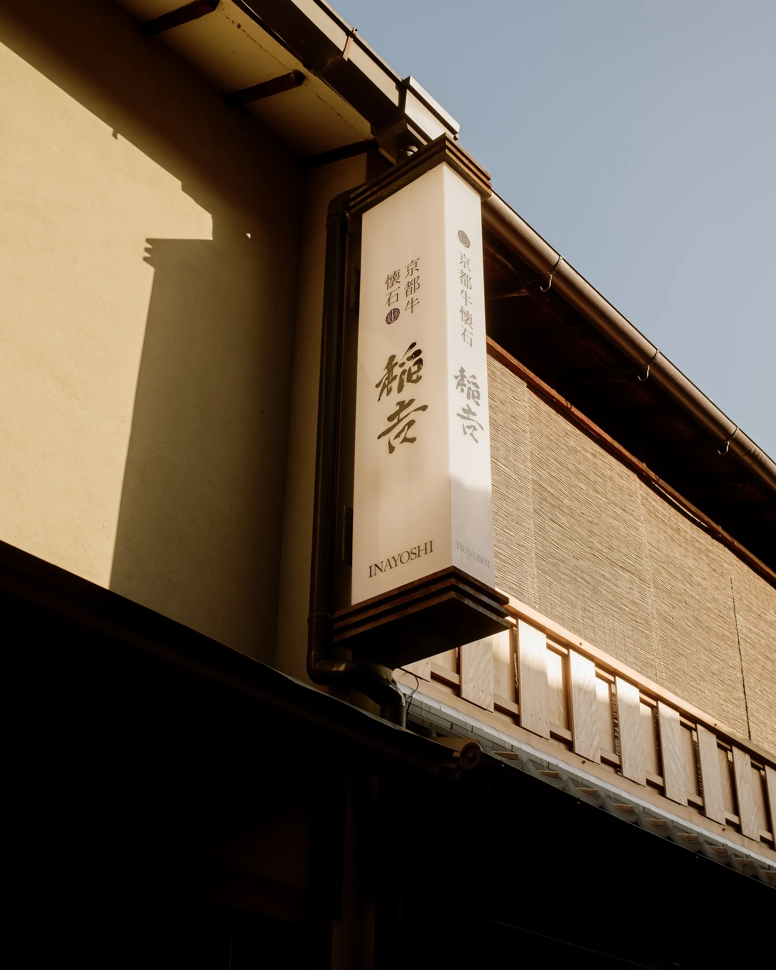 Hanging sign above a Kyoto storefront, warm light on a dark wooden facade