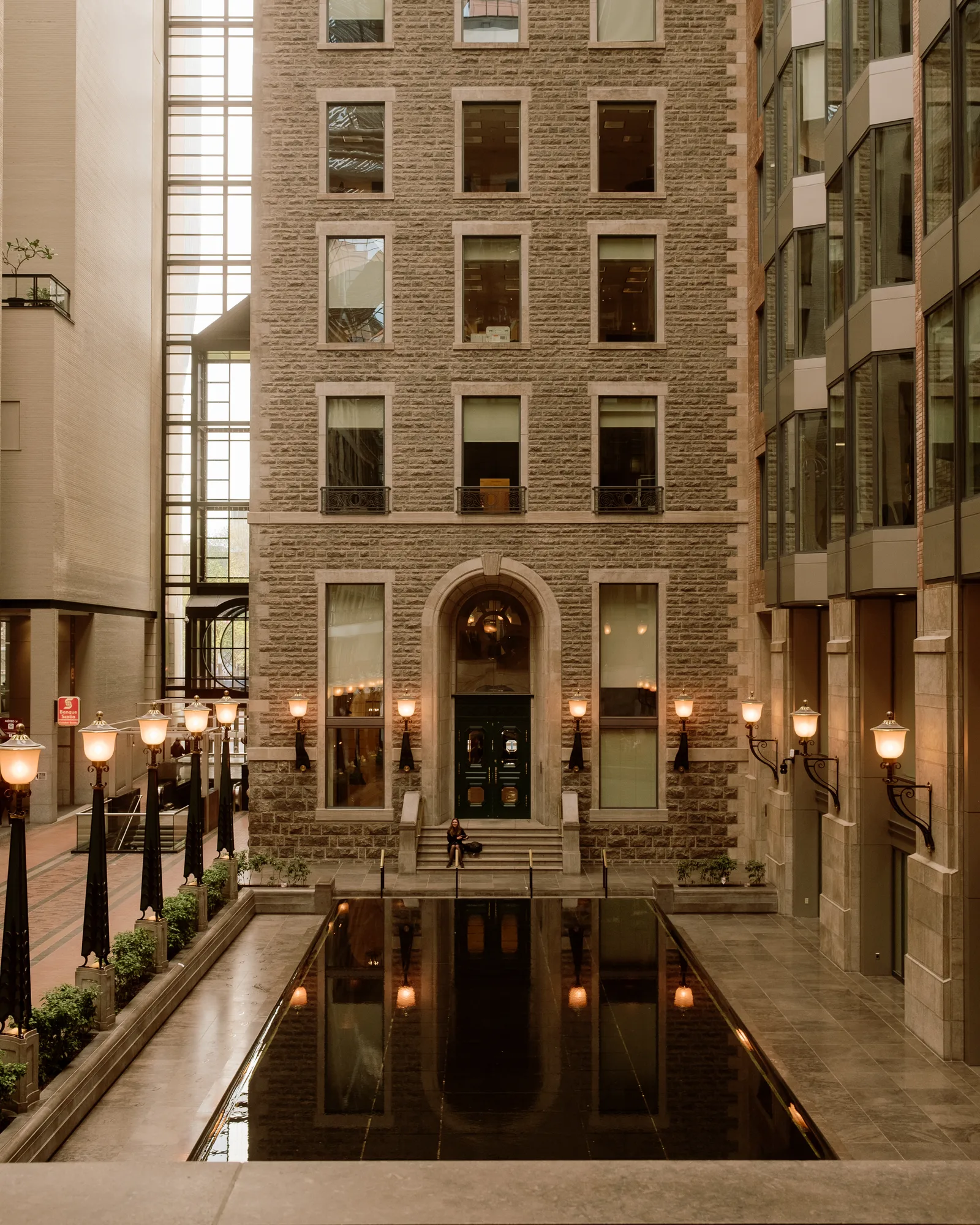 Stone office building glowing with lamps above a dark reflecting pool, Montreal