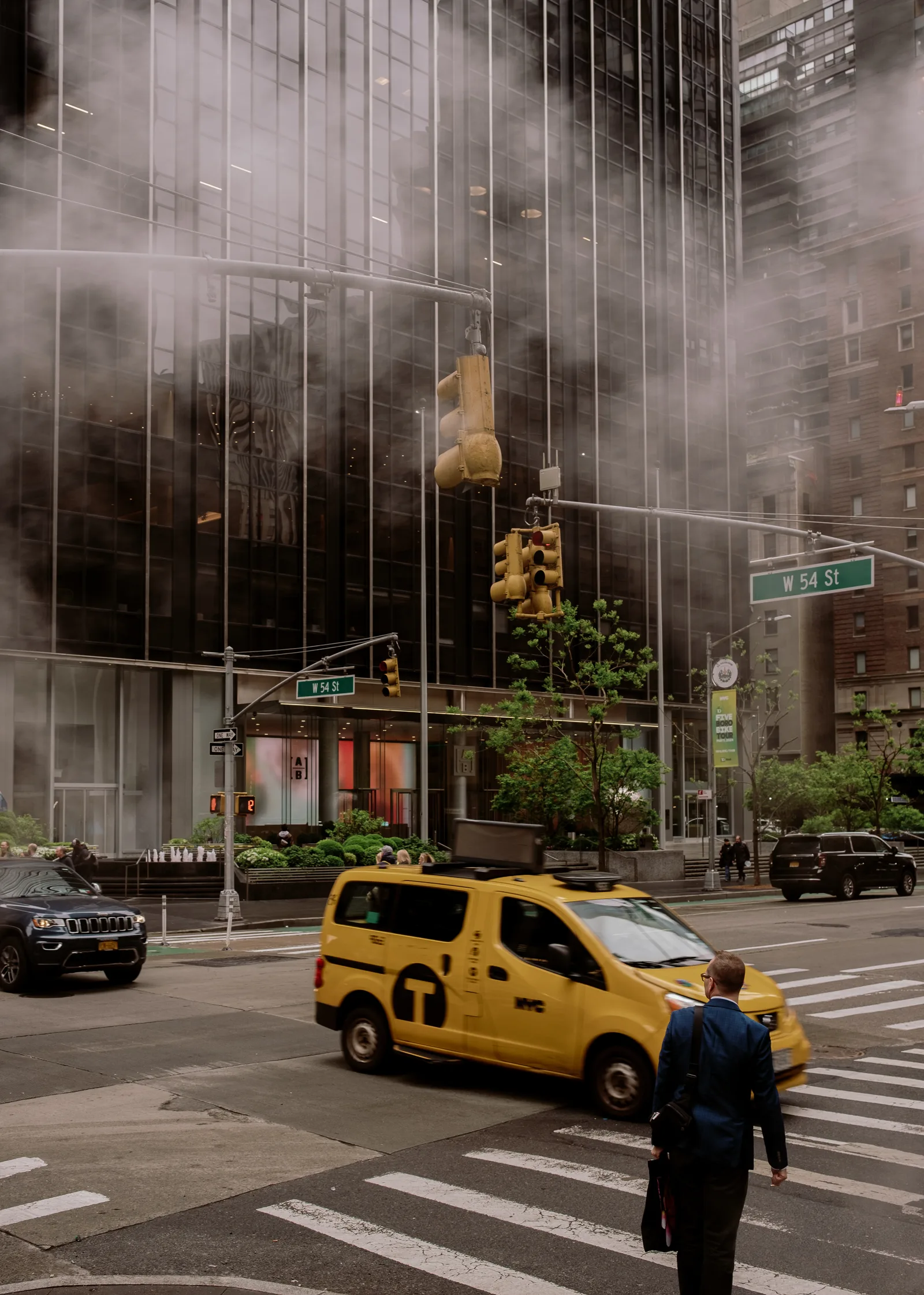Yellow taxi and a pedestrian crossing a Manhattan intersection below steaming glass towers