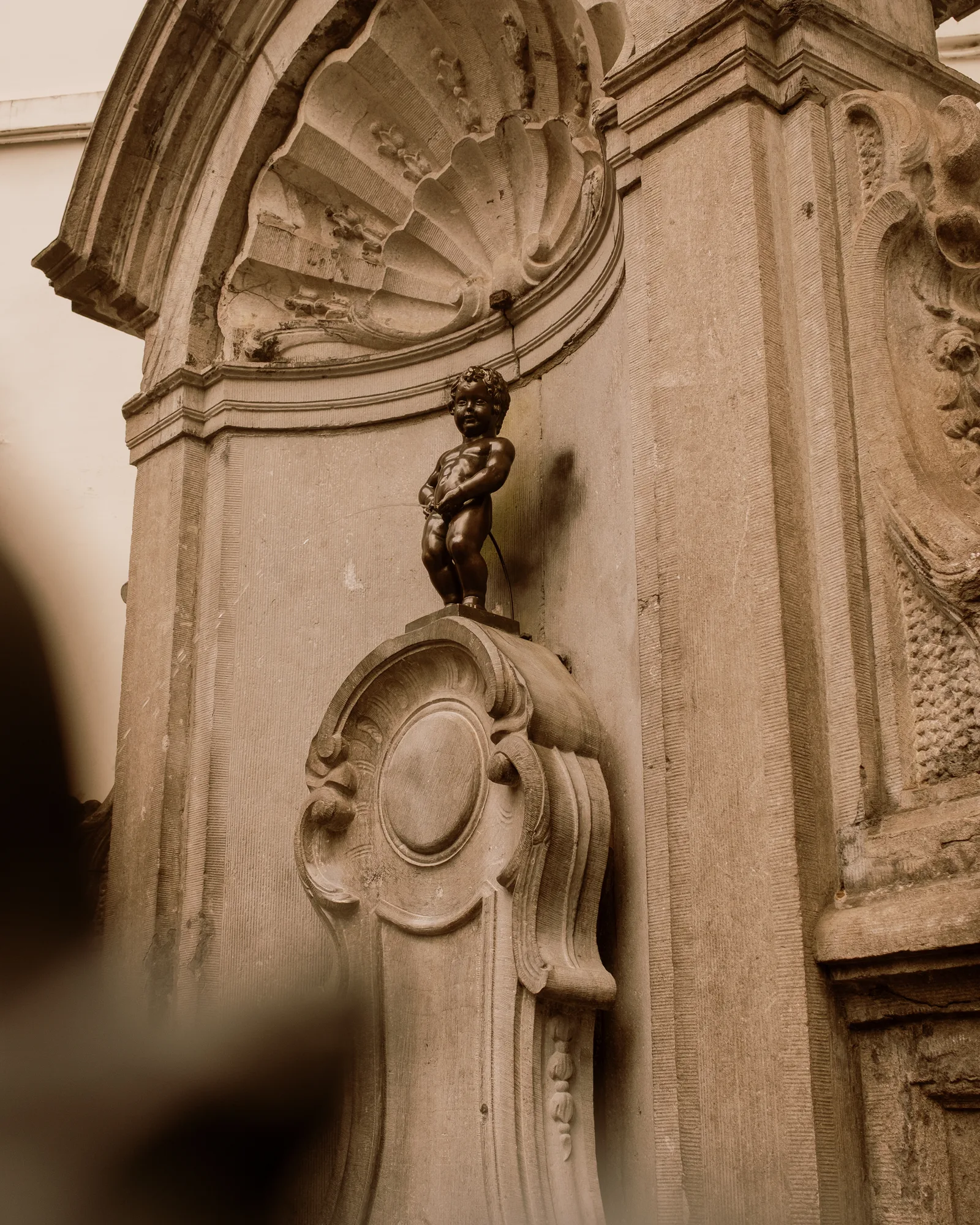 Manneken Pis, the small bronze fountain figure, in its stone shell niche, Brussels