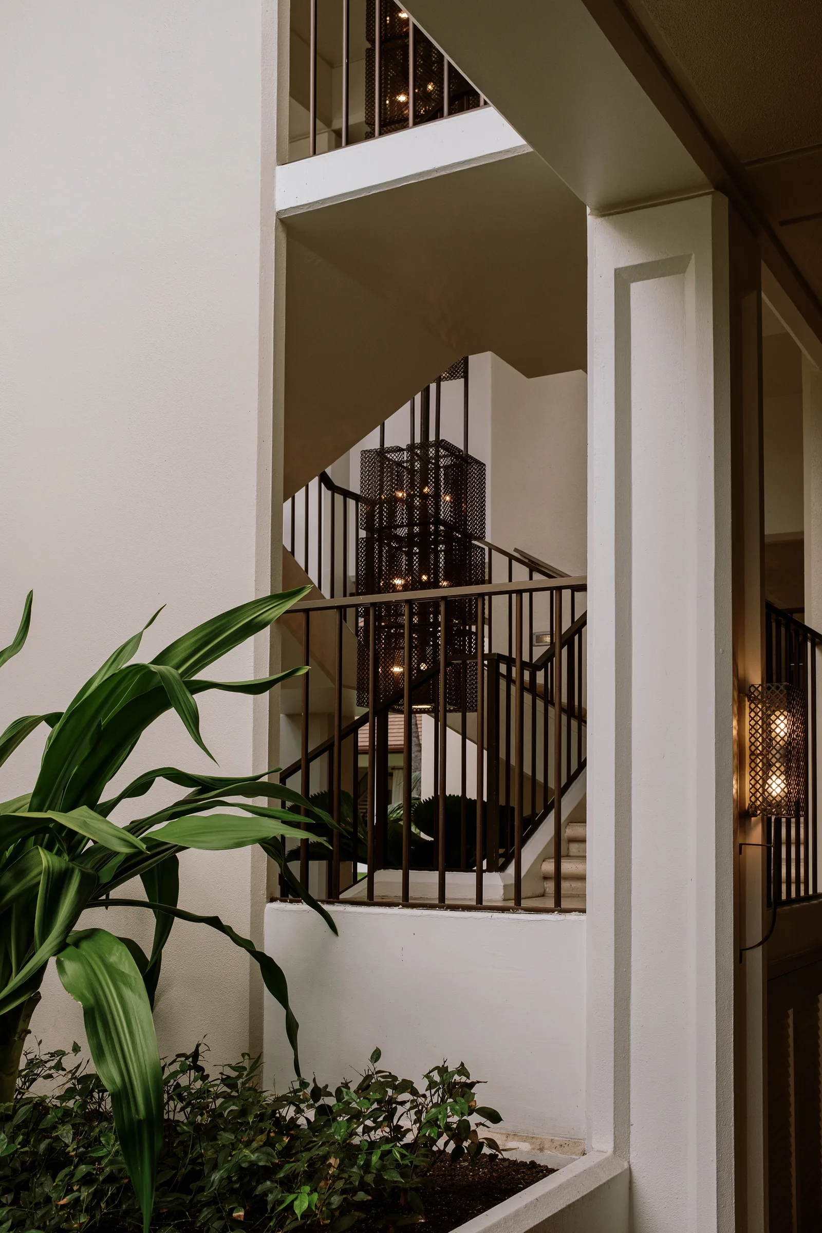 Iron-railed stair landing beside a white column and green plants, Oahu