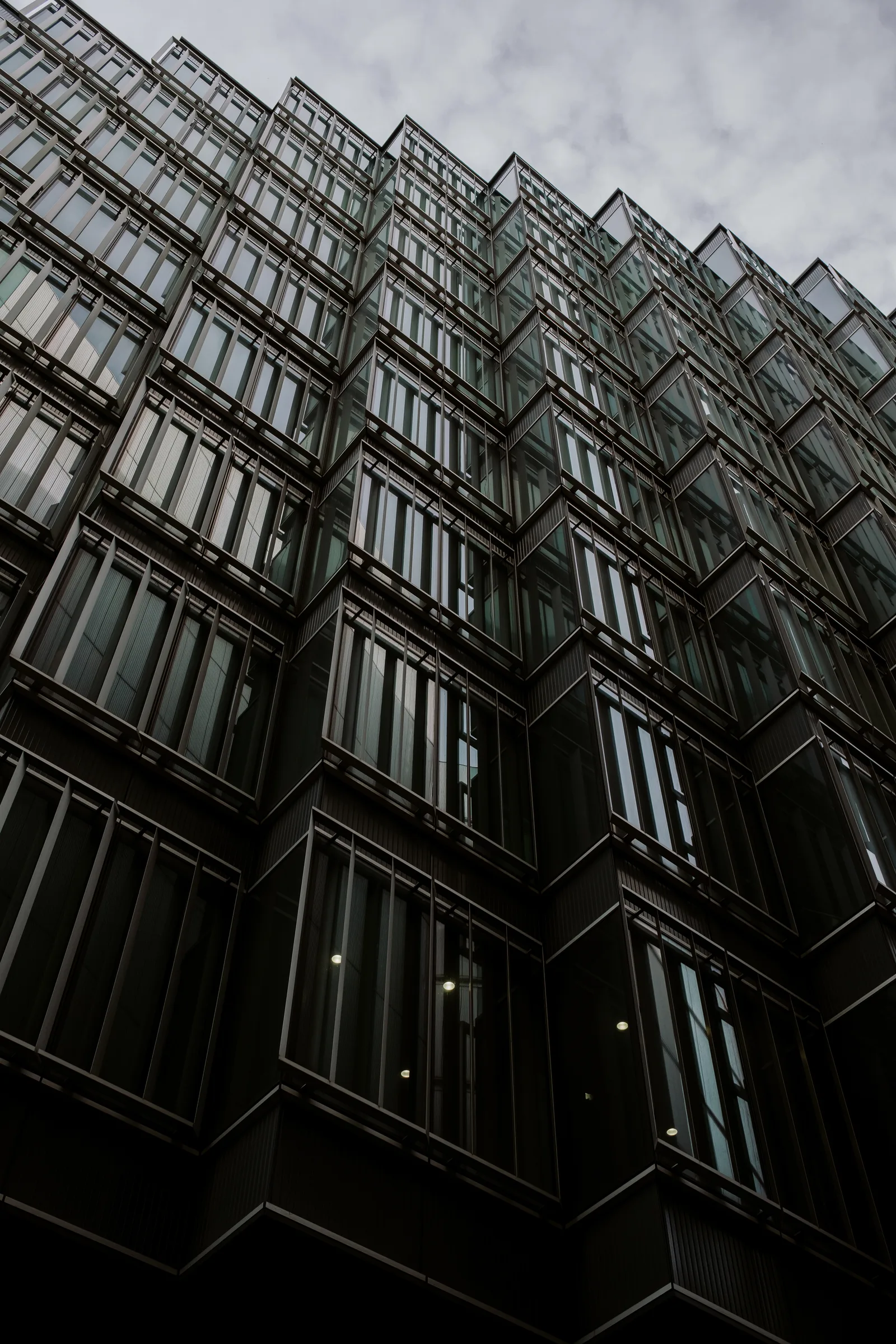 Stacked glass bays of an office facade seen from below against a cloudy sky, London
