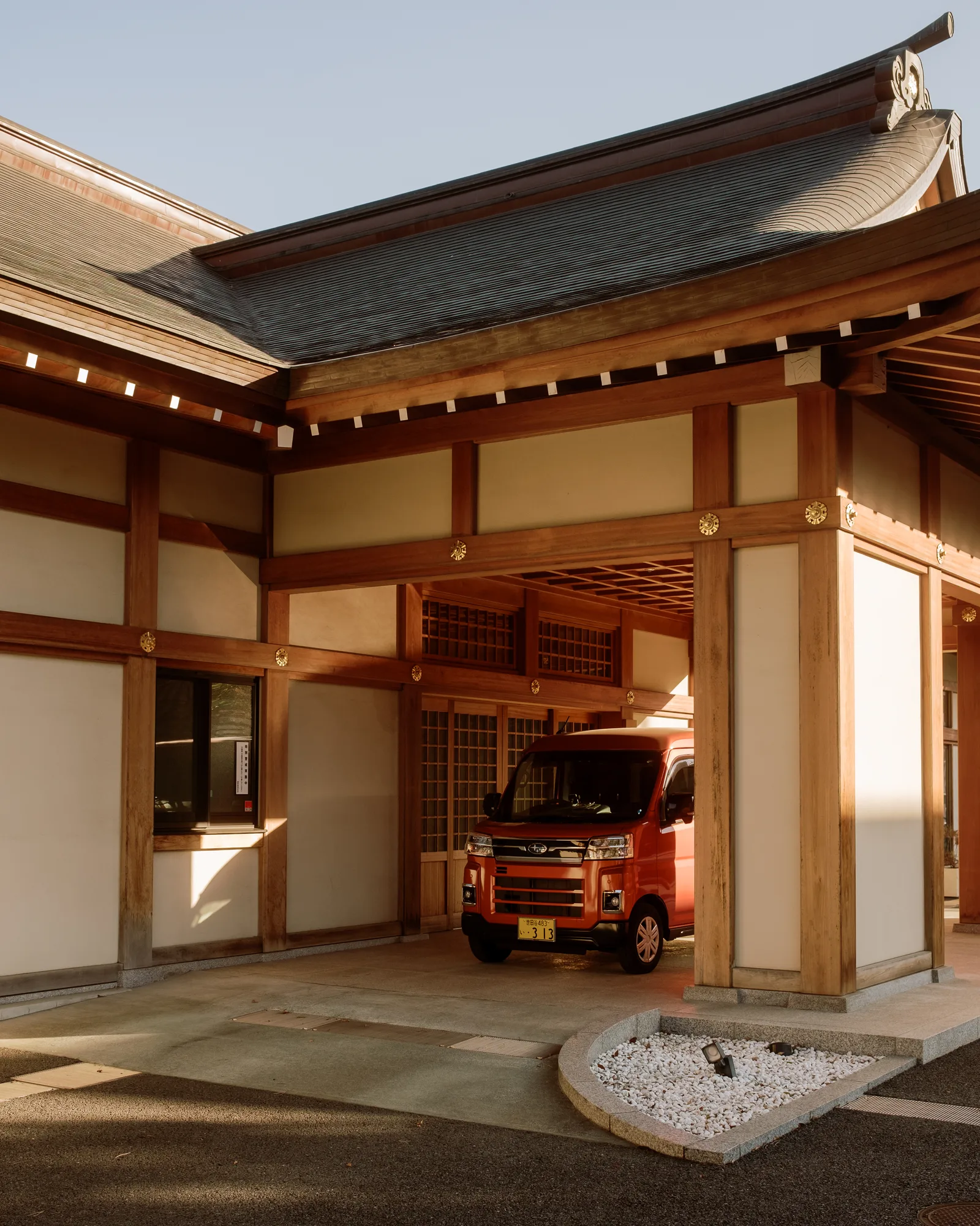 Wooden temple building sheltering a red van beside a raked gravel patch, Tokyo