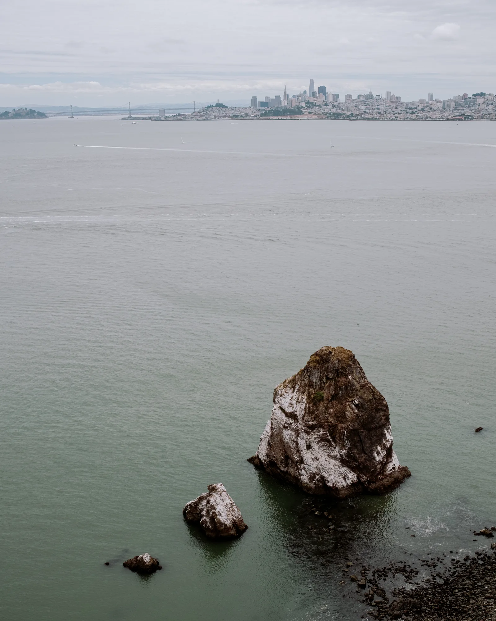 Sea stack rising from calm bay water with the San Francisco skyline in the distance