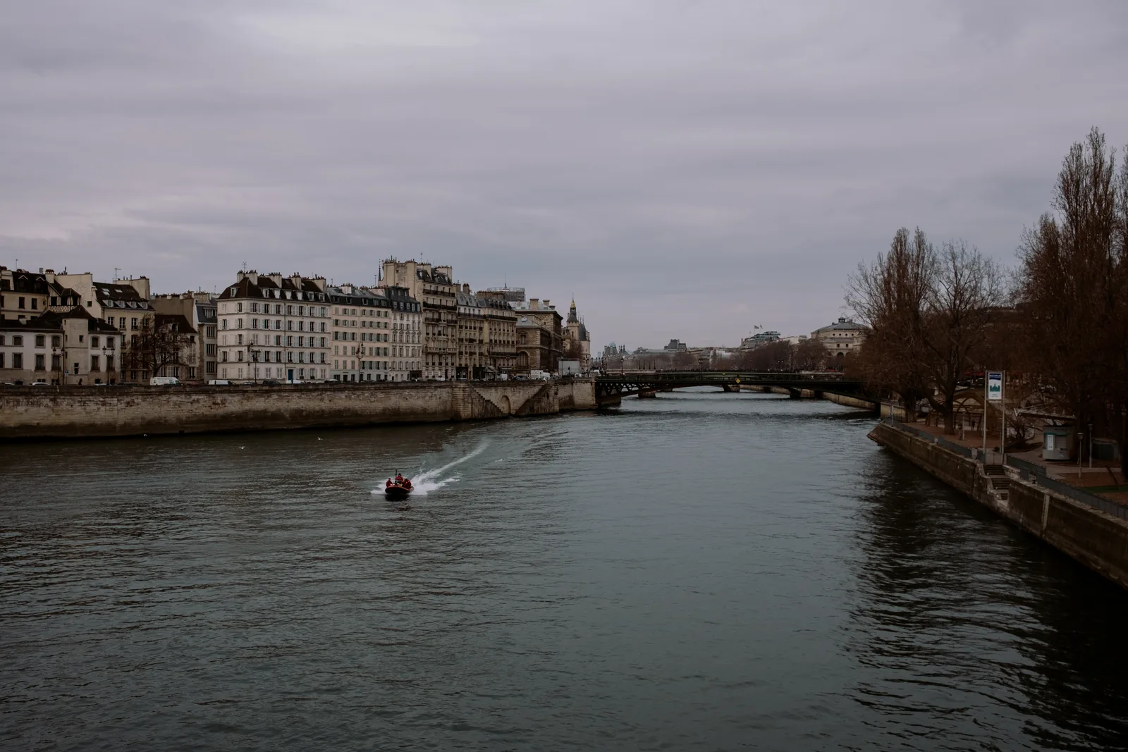 A boat leaving a wake on the Seine lined with stone buildings, Paris