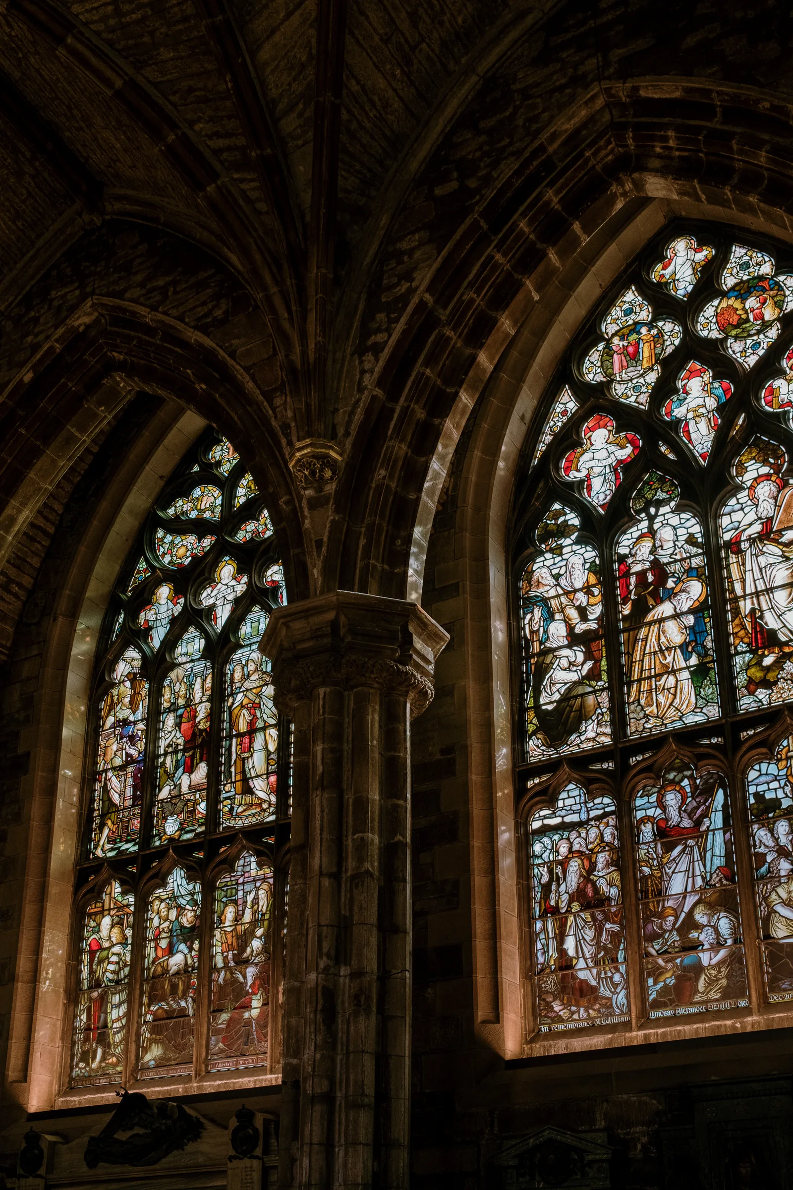 Stained-glass windows framed by dark stone arches in a Gothic Edinburgh interior