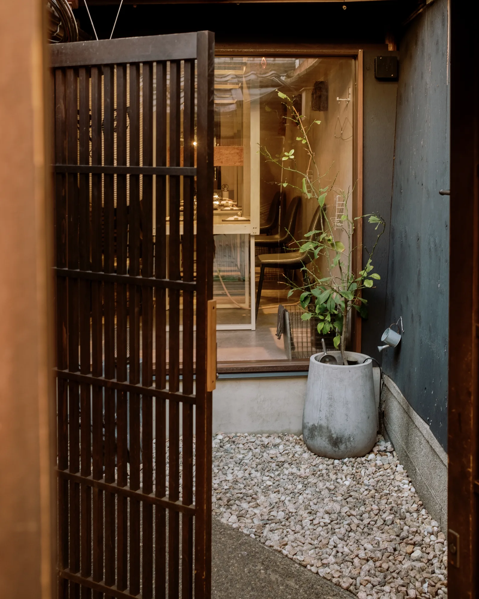 Open wooden latticed door to a Kyoto shop with a potted plant and raked white gravel