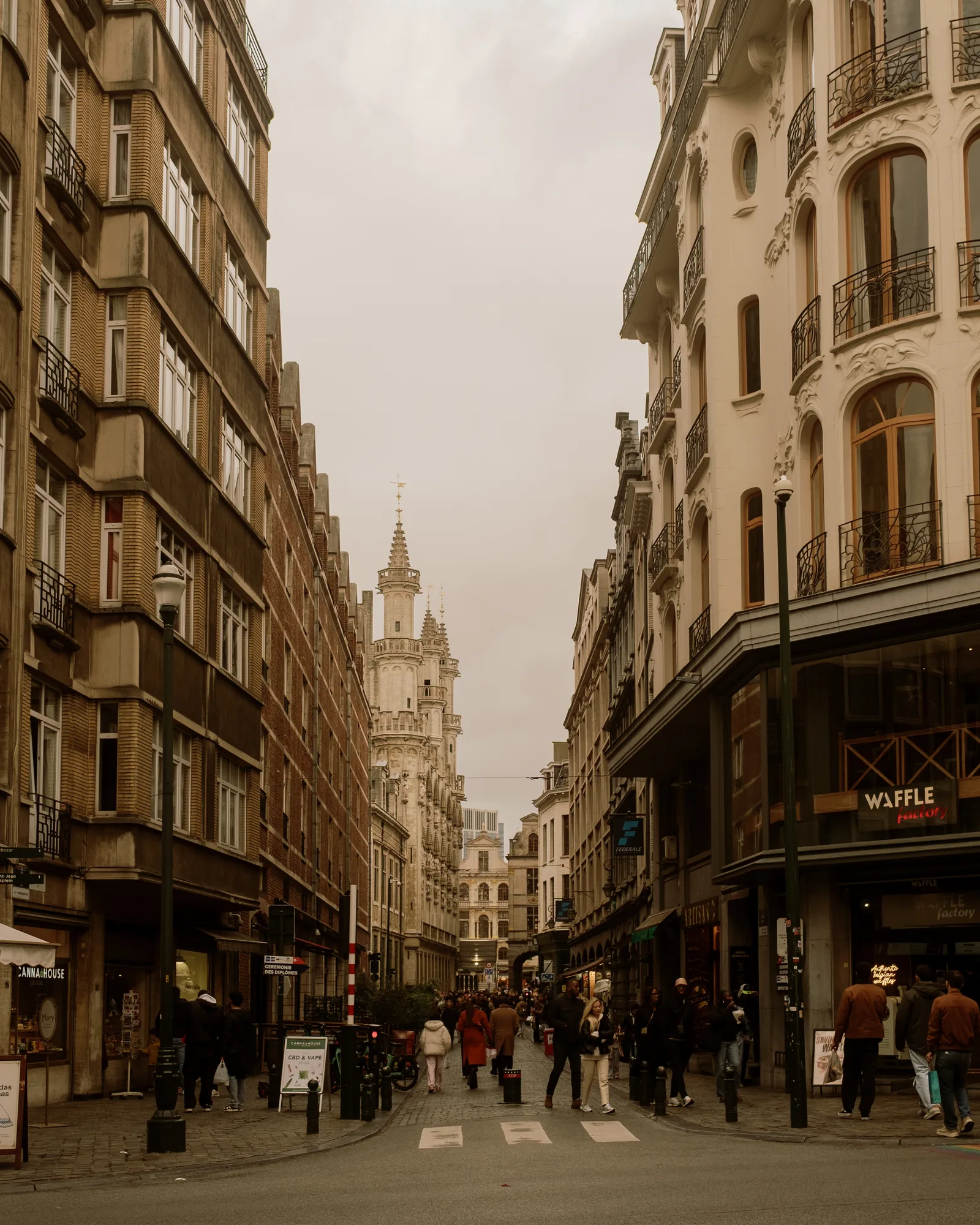 Brussels street between tall buildings leading to a distant clock tower, pedestrians below