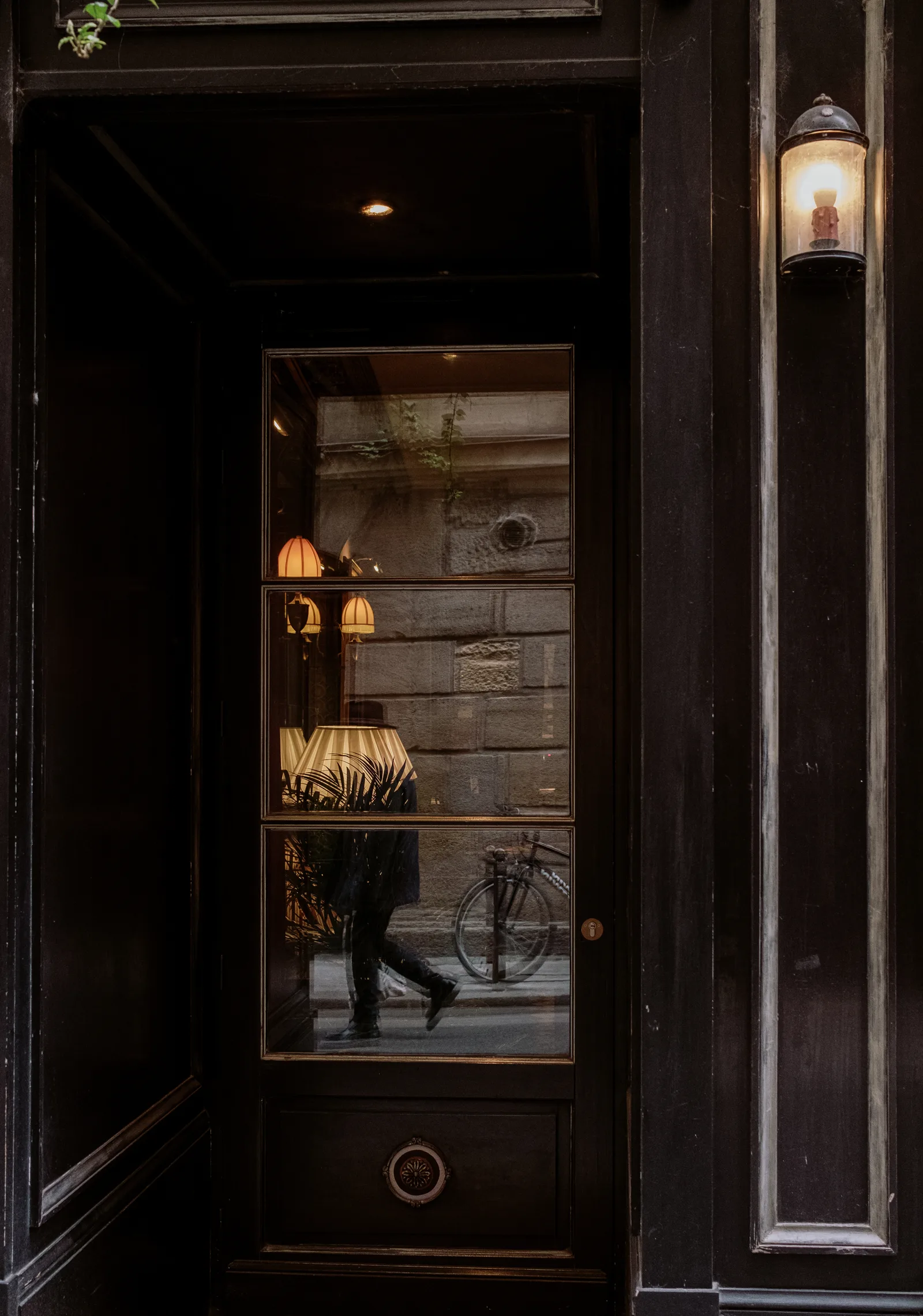 Dark restaurant doorway with a lantern and a passer-by seen through glass, Paris