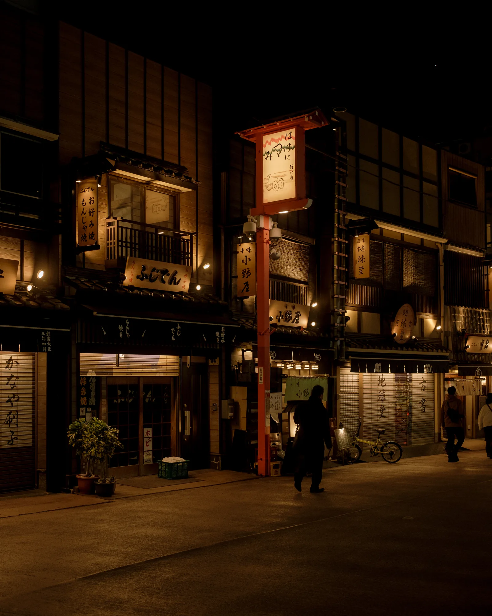 Wooden storefronts and a red hanging sign on a lit Asakusa street at night, Tokyo