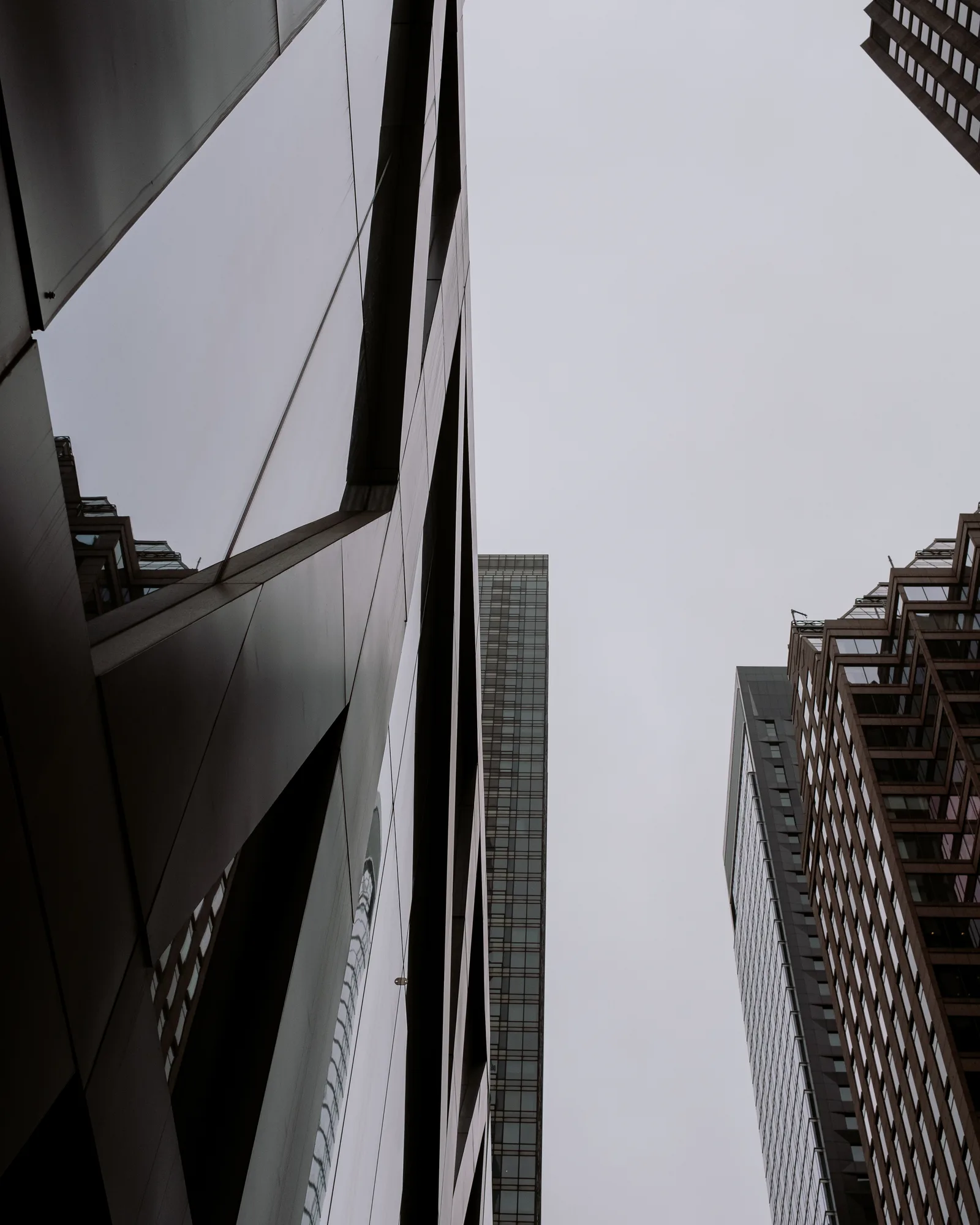 Looking up between dark glass towers to a gray sky, New York