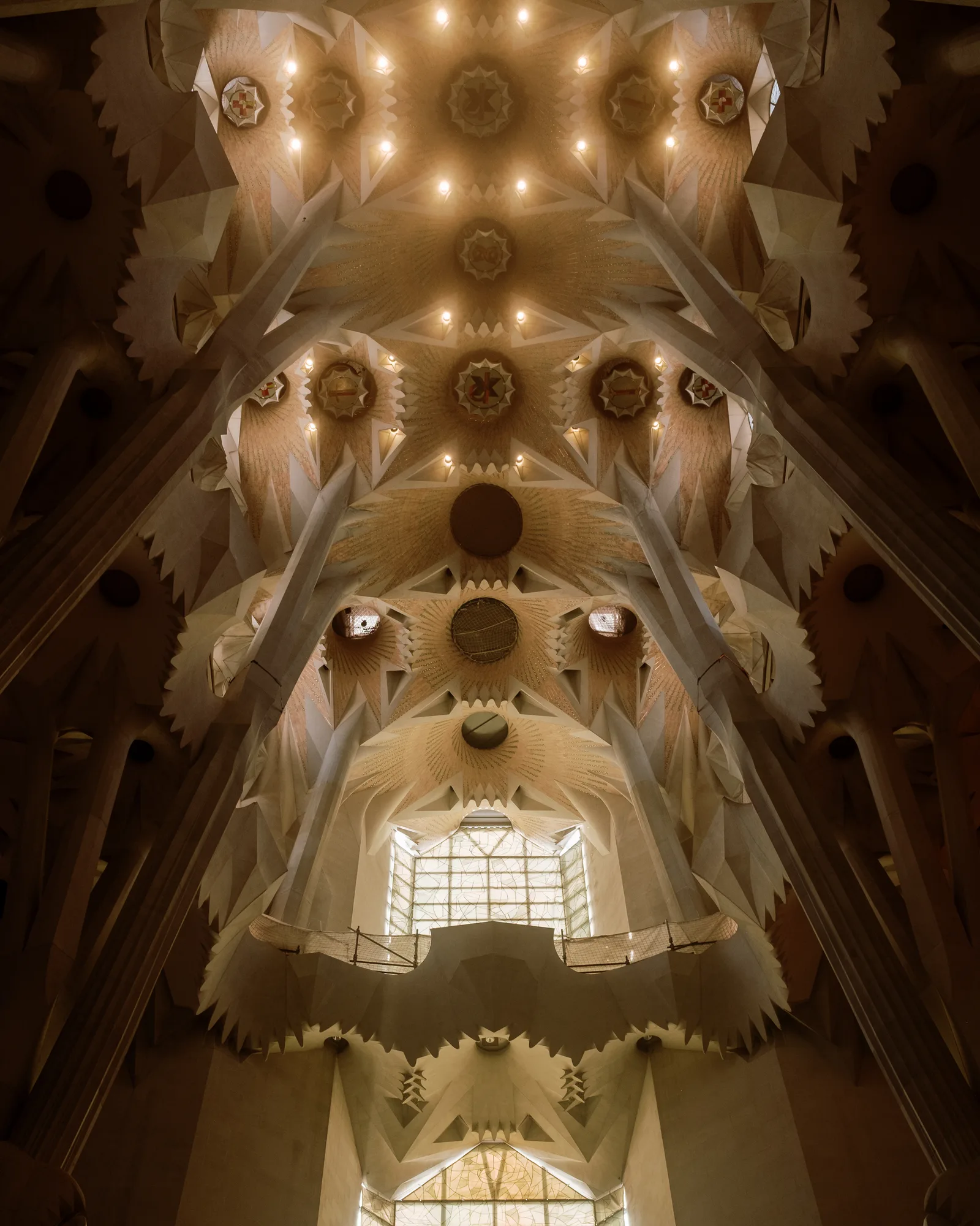 Looking up the nave of the Sagrada Família toward a bright window, branching columns and vaults overhead