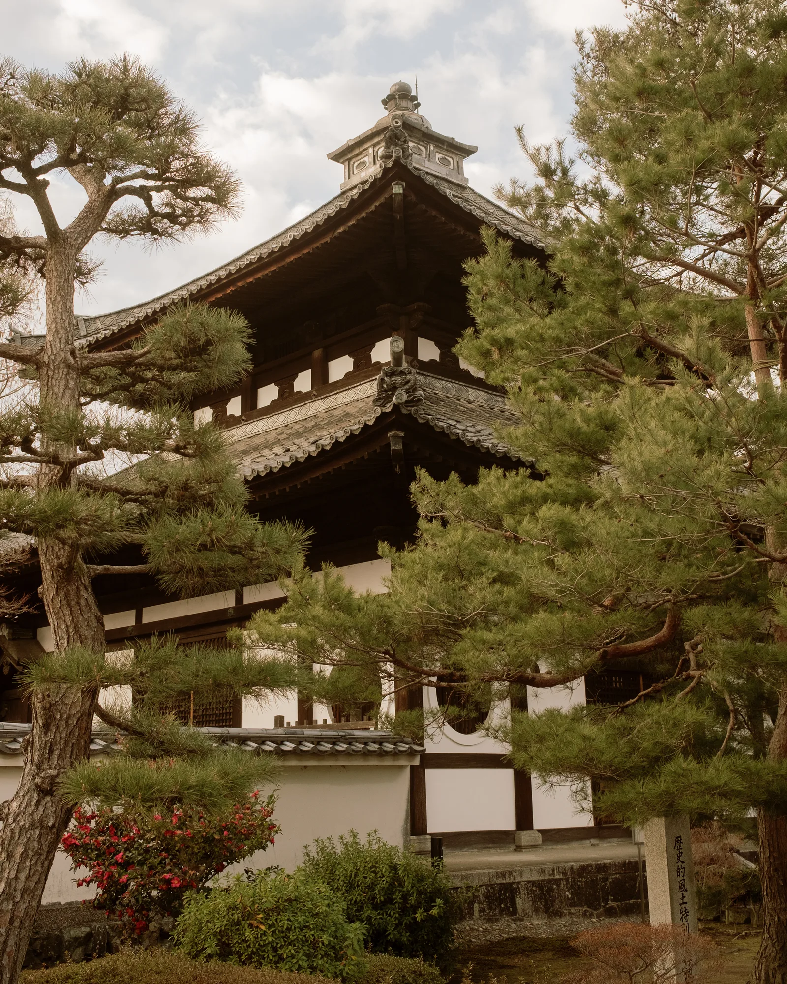 Multi-tiered temple roof framed by pine trees and a white garden wall, Kyoto