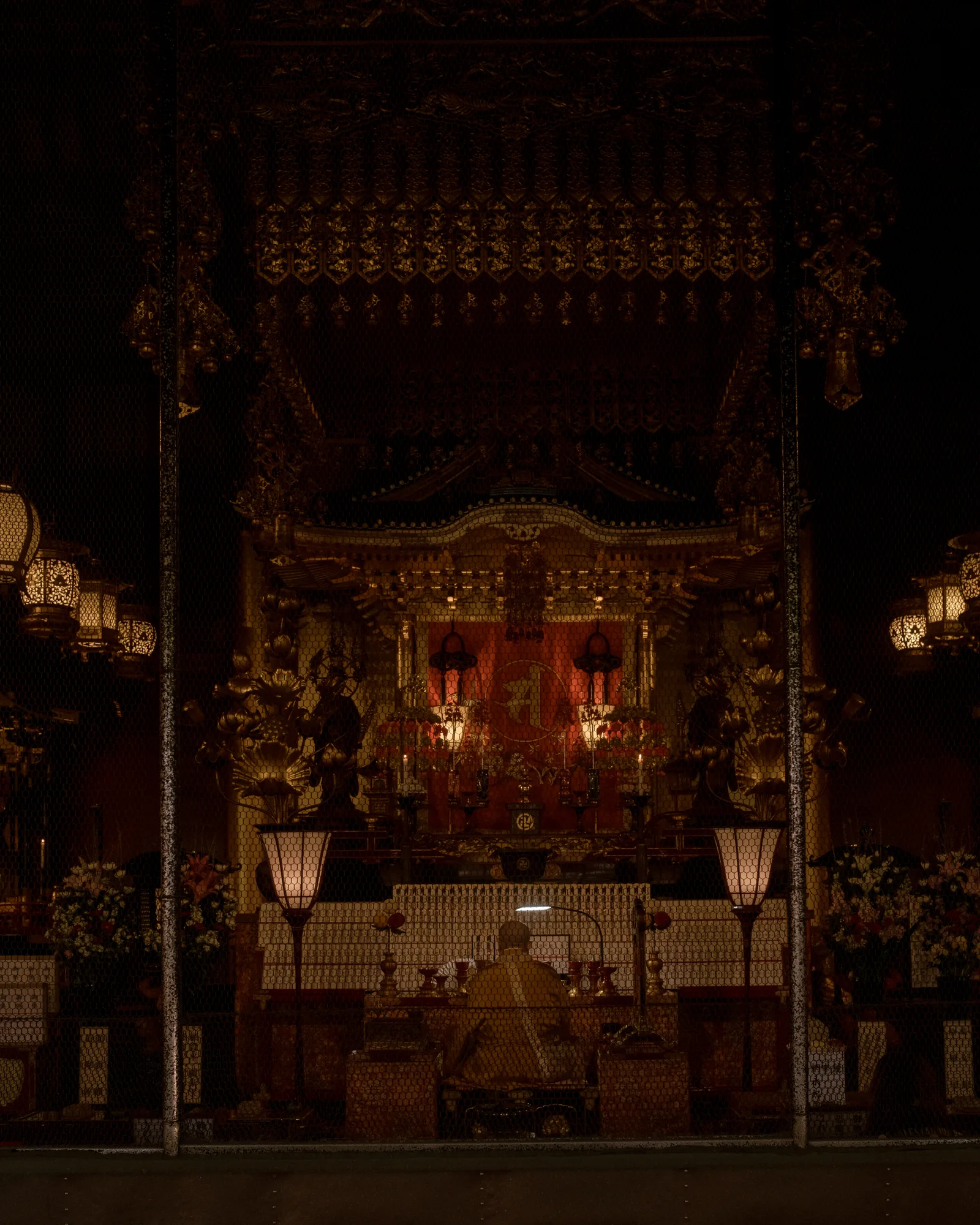 Monk seated before a gilded altar in a dark temple hall, Tokyo