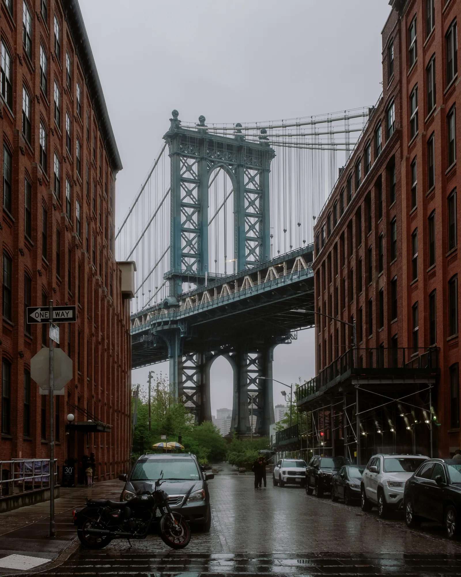 Manhattan Bridge framed by red-brick warehouses on a rainy DUMBO street, New York
