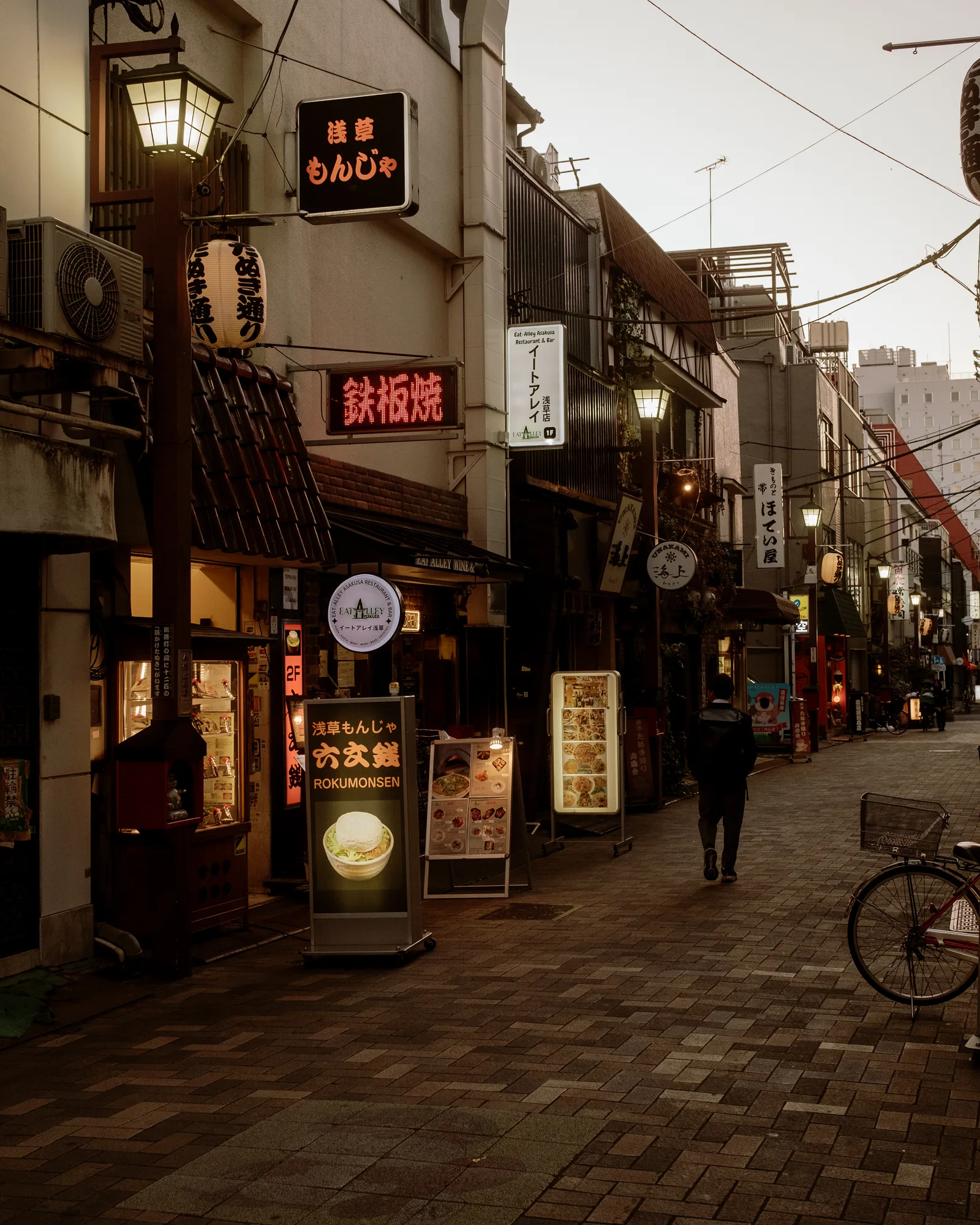Asakusa lane with glowing signs and lanterns, a pedestrian walking away, Tokyo