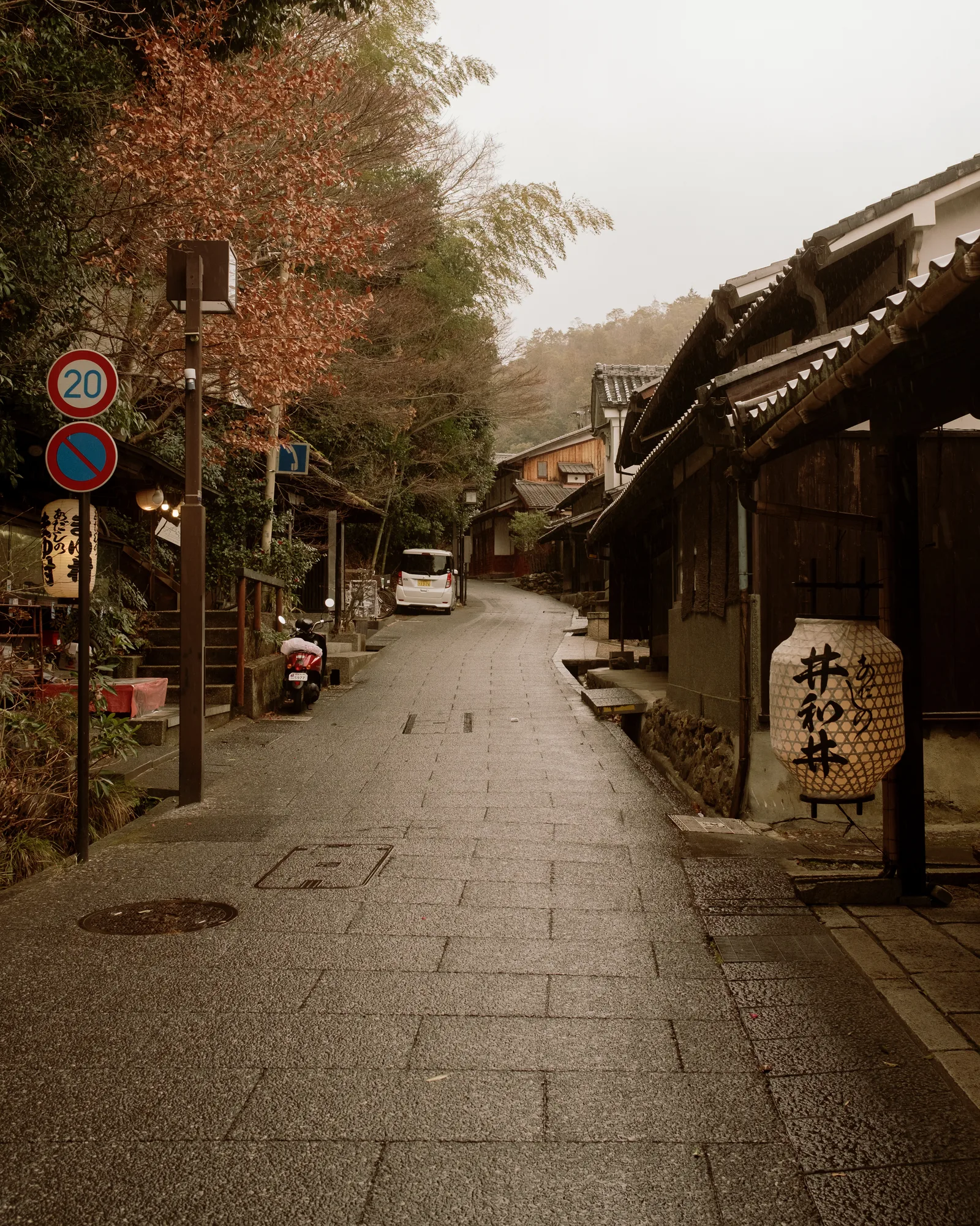 Empty stone-paved street rising past traditional wooden buildings and a paper lantern, Kyoto