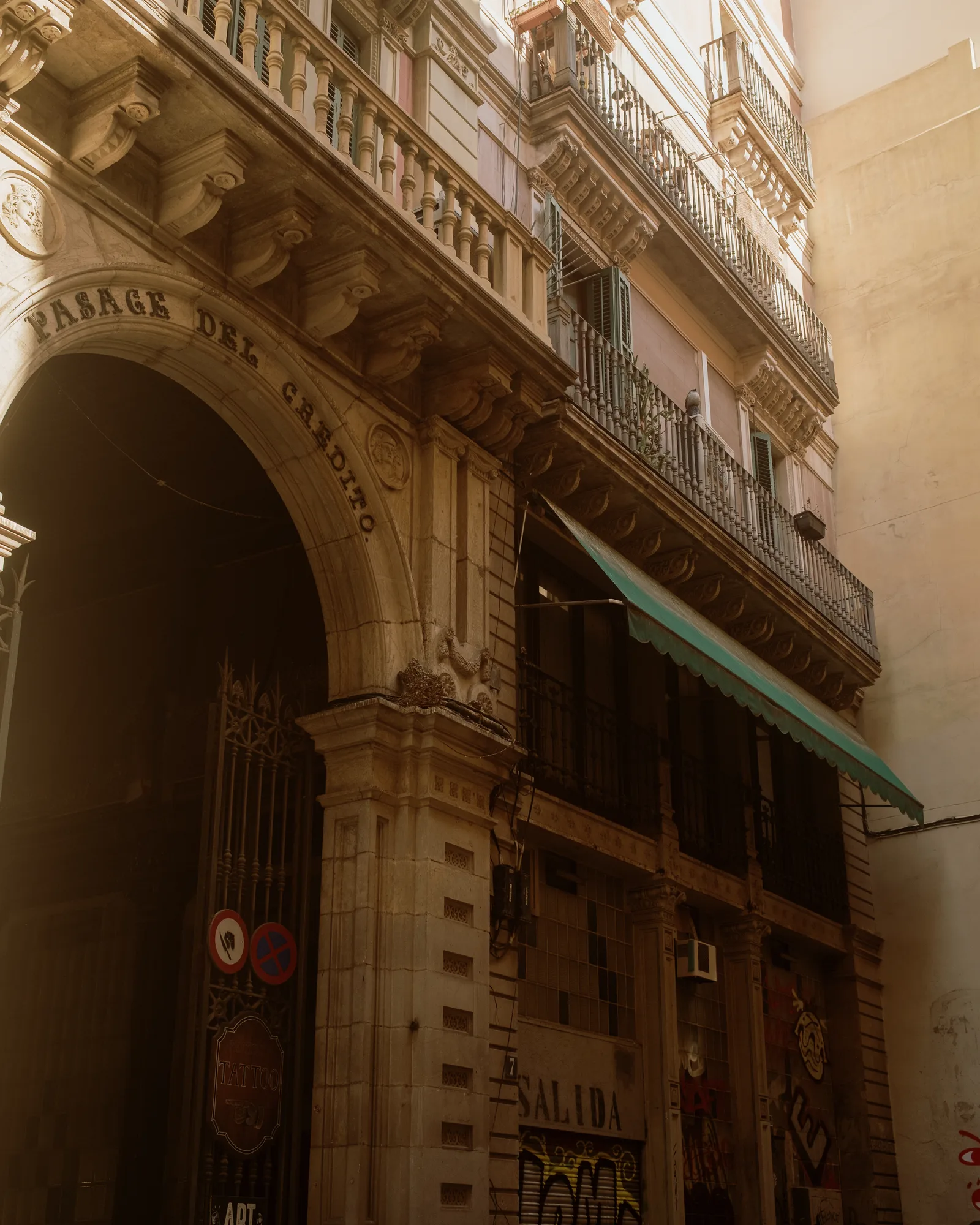 Arched passage entrance under wrought-iron balconies and a green awning, Barcelona