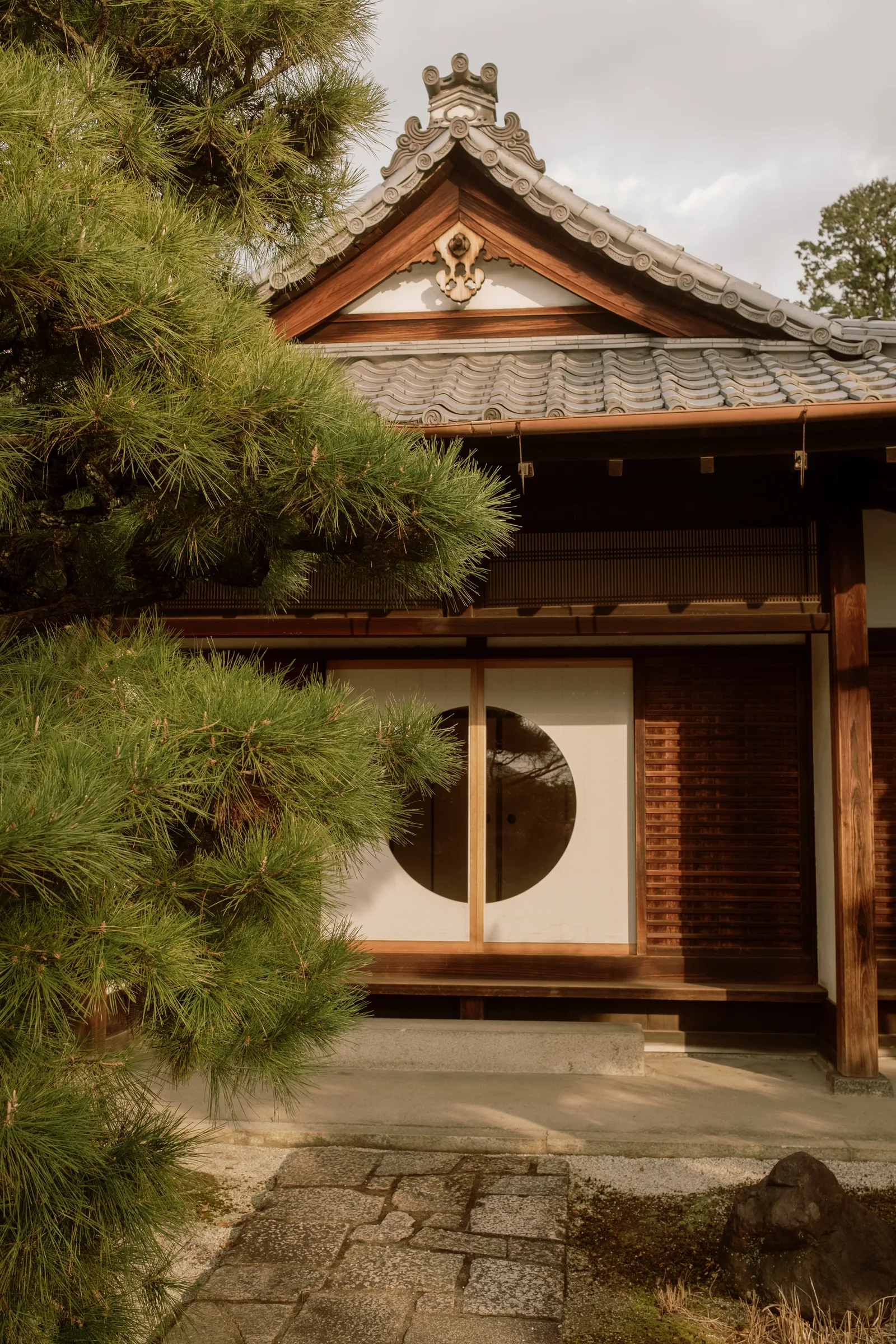 Tiled temple building with a round window beside a pine tree, Kyoto